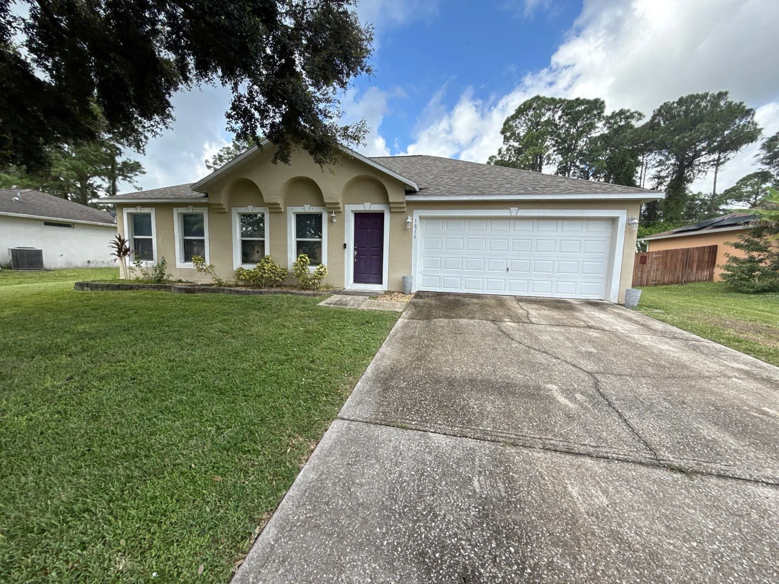 Exterior Painting in Bayside Lakes, Florida. Single-storey stucco house painted cream with white trim, arched entry, plum front door and white garage door, seen from the driveway.