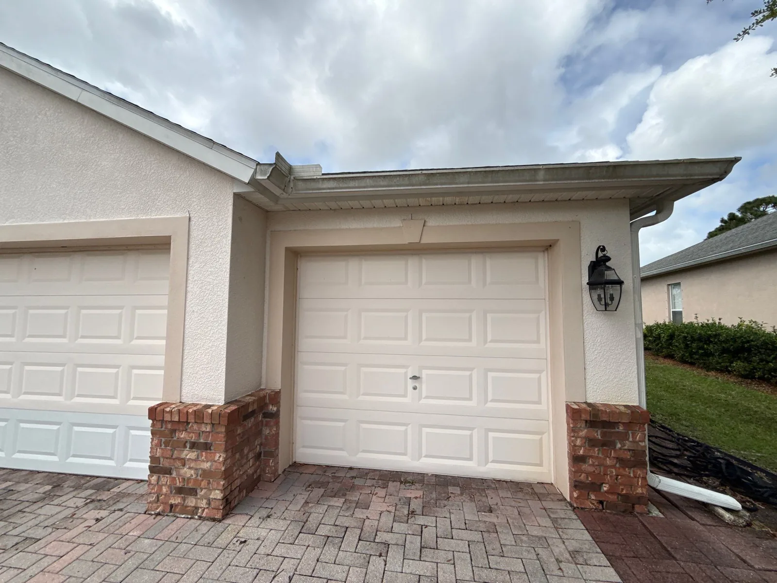 Exterior Painting in Bayside Lakes, Florida. Single-car garage bay with cream stucco walls, white garage door and brick veneer columns over a paver driveway.