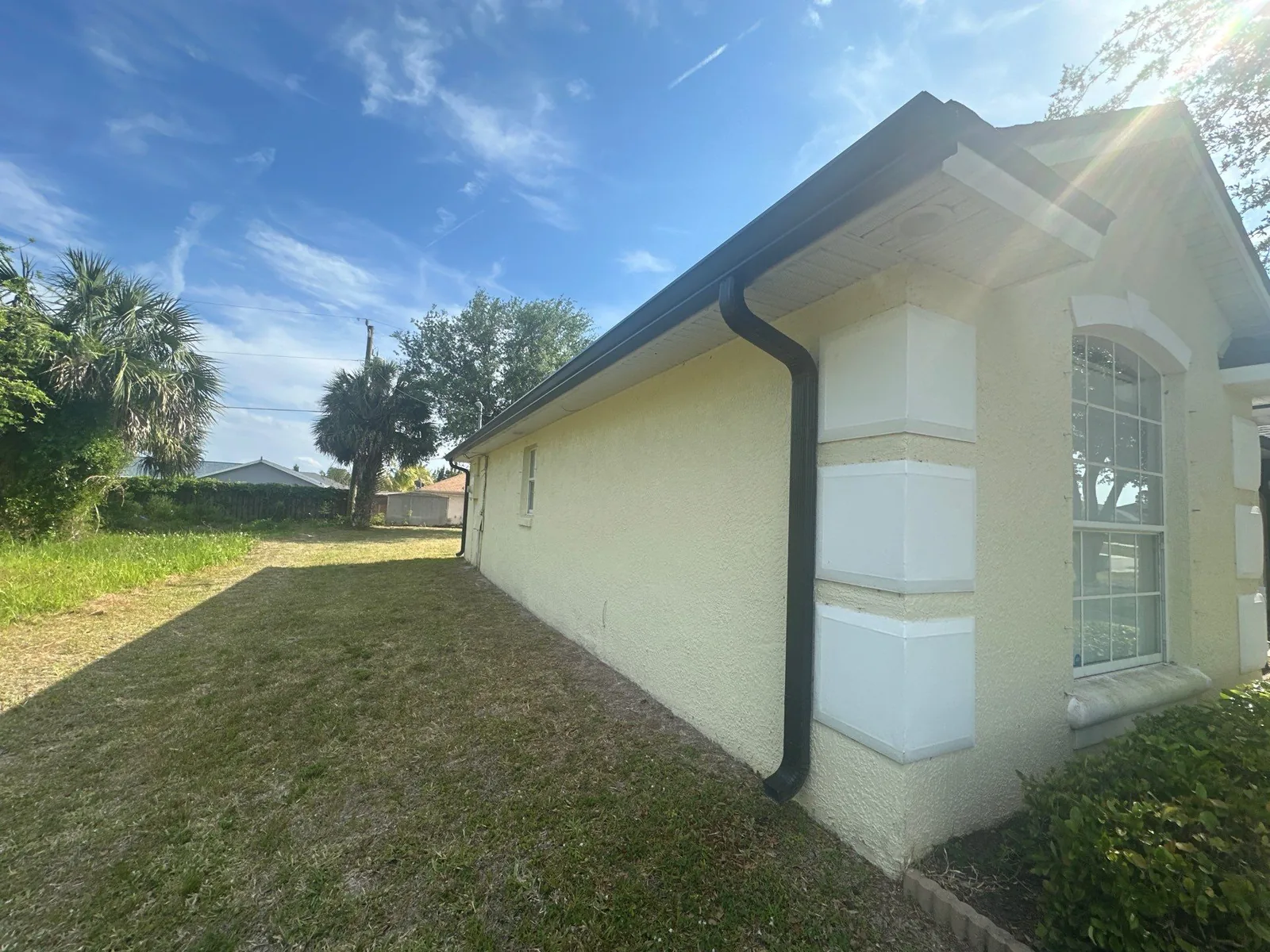 Exterior Painting in Bayside Lakes, Florida. Side elevation of a cream stucco home with white painted quoin corner detail and an arched window.