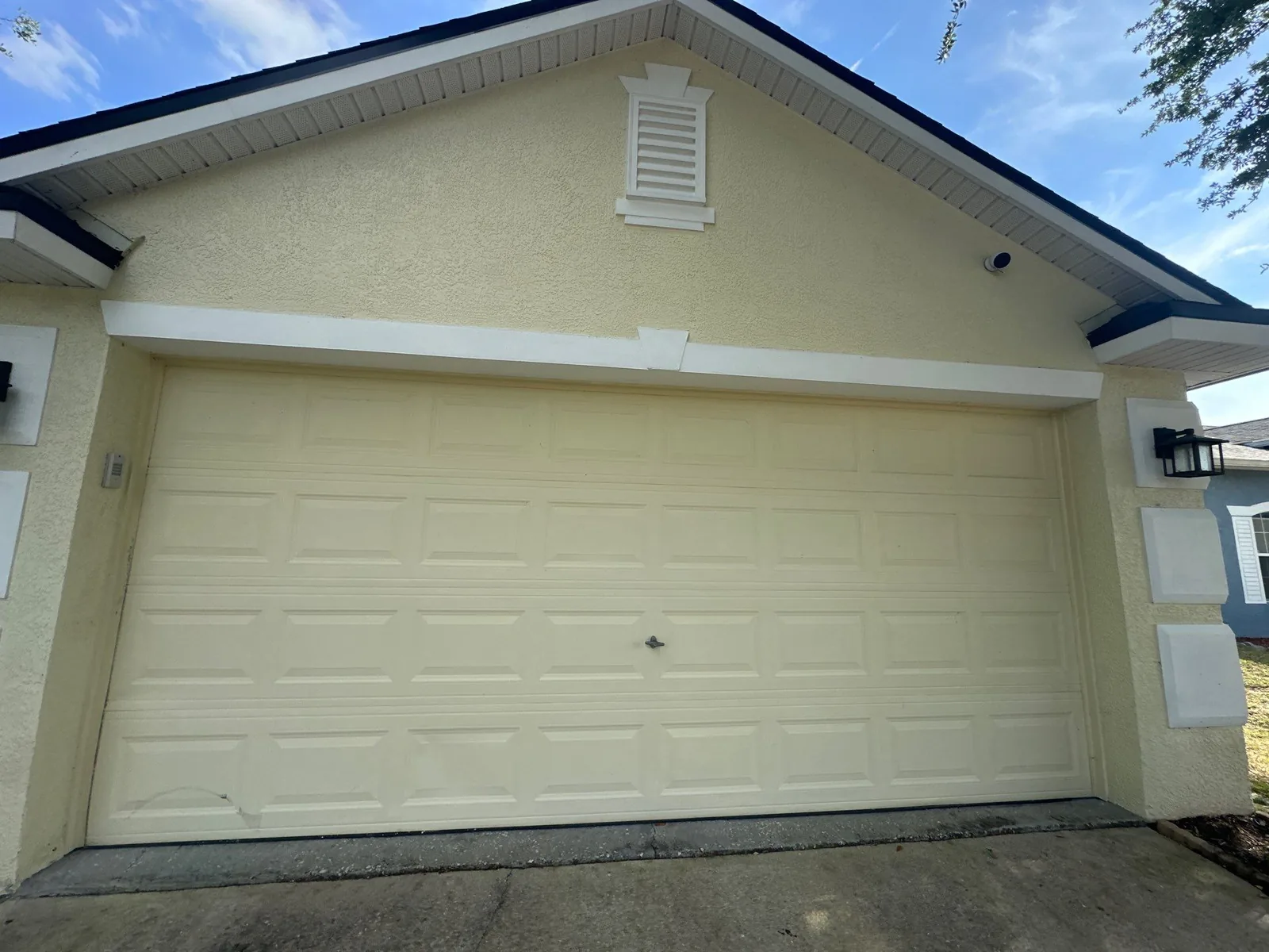 Exterior Painting in Bayside Lakes, Florida. Freshly painted cream double garage door with white trim and gable vent above.