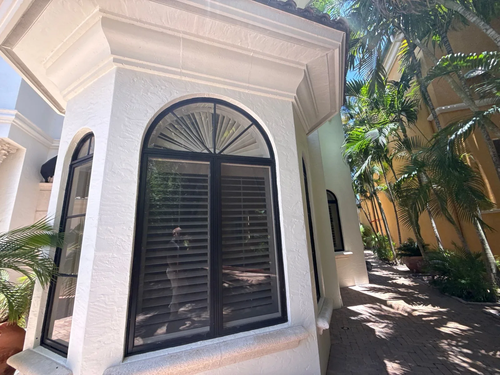 Exterior Painting in Boca Raton, Florida. White stucco bay window with an arched dark-framed window, louvered shutters and white cornice trim.