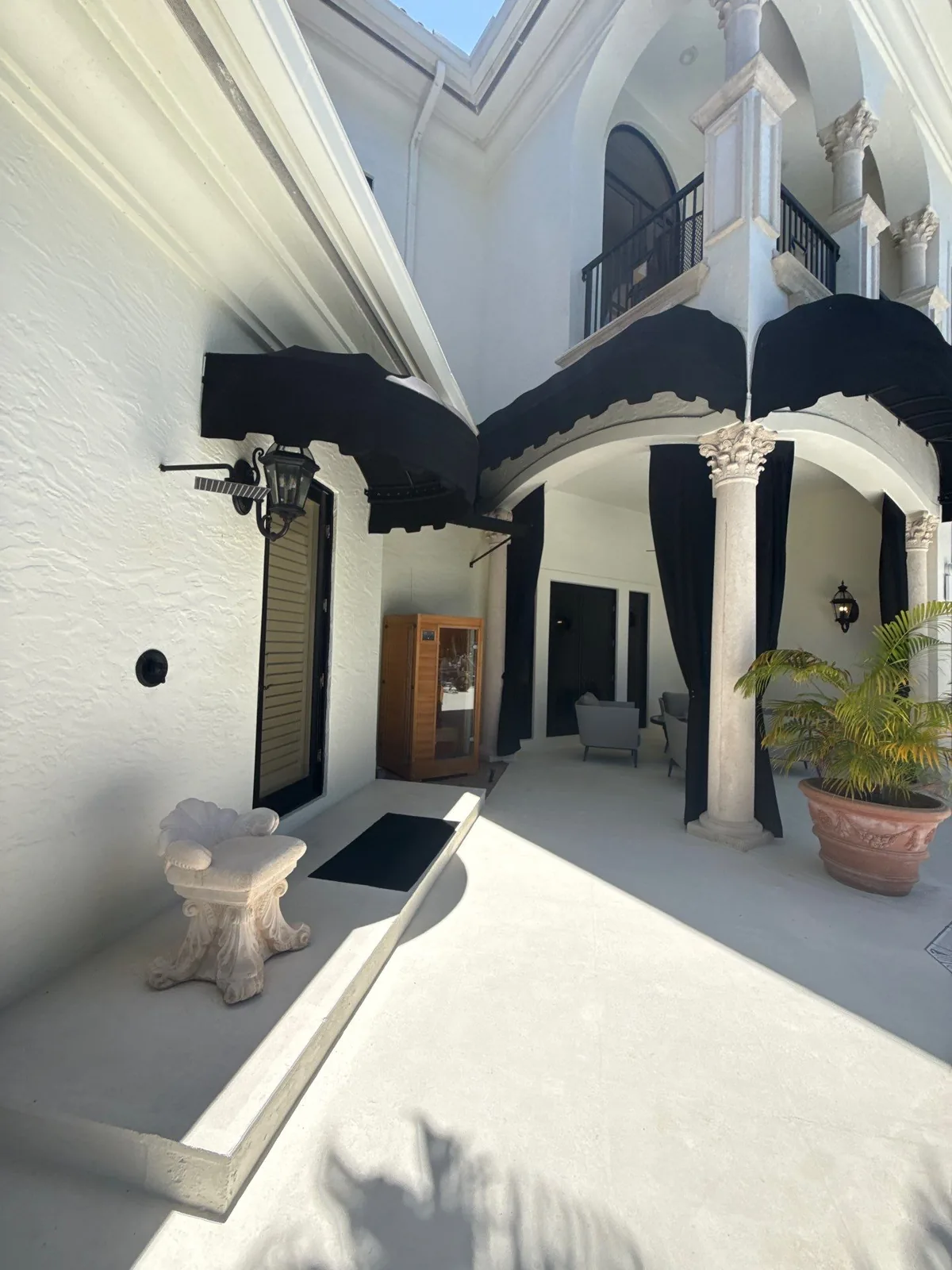Exterior Painting in Boca Raton, Florida. Courtyard with white stucco walls, black awnings, columns and outdoor seating.