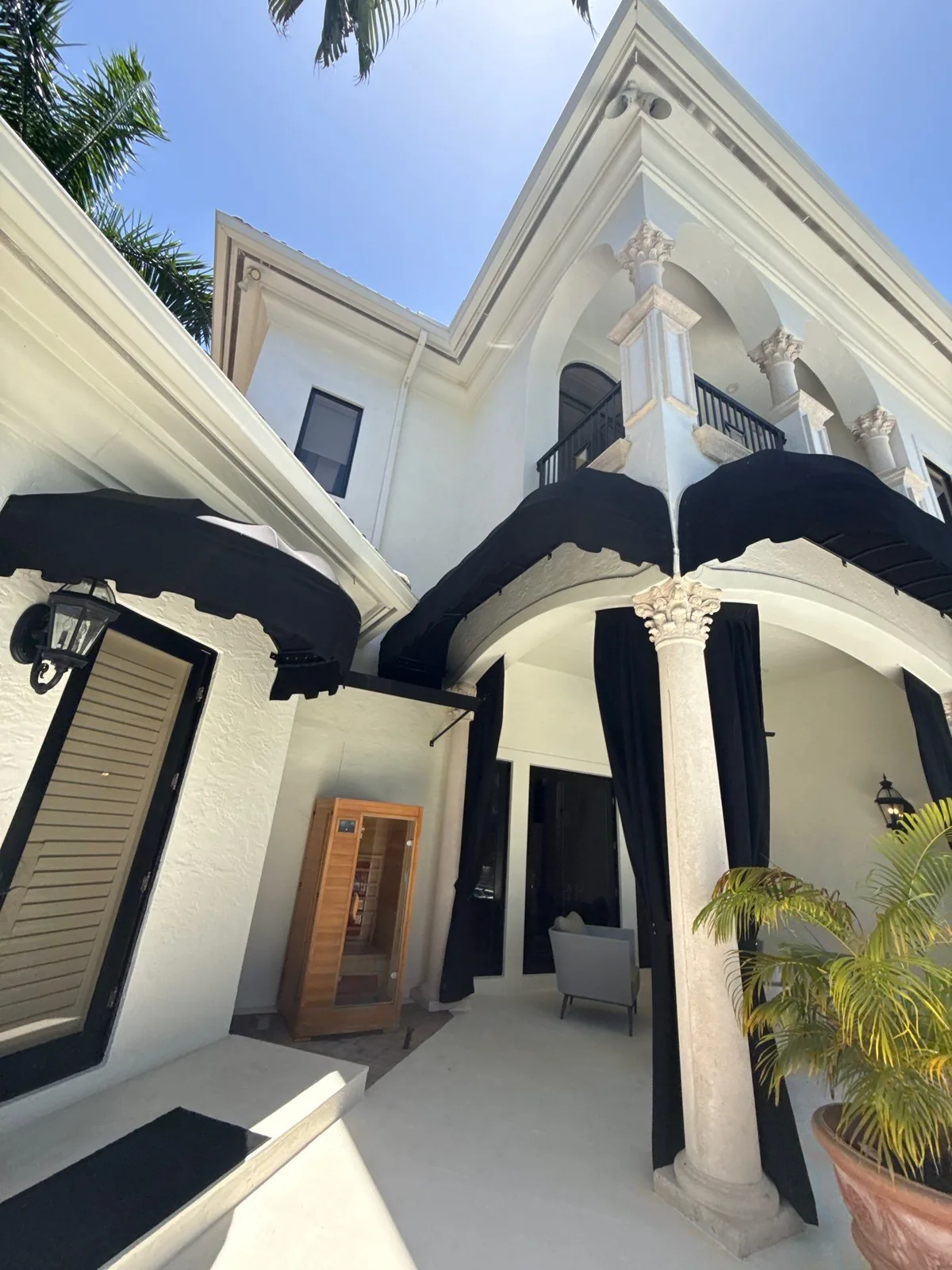 Exterior Painting in Boca Raton, Florida. Two-storey white stucco courtyard elevation with black awnings, columns and an upper balcony.