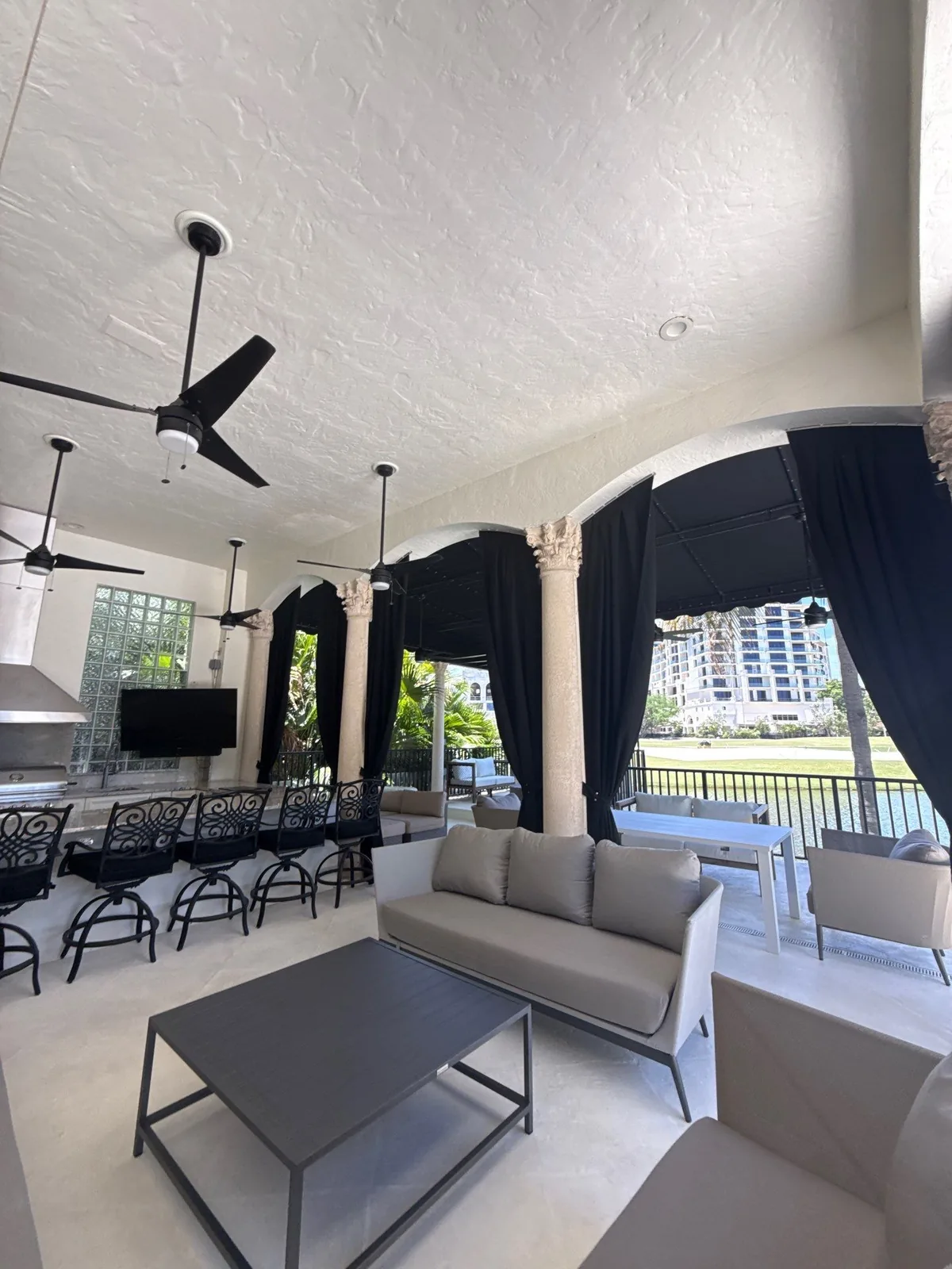 Exterior Painting in Boca Raton, Florida. Covered outdoor living area with a painted ceiling, columns, ceiling fans, black drapes, outdoor kitchen and seating.