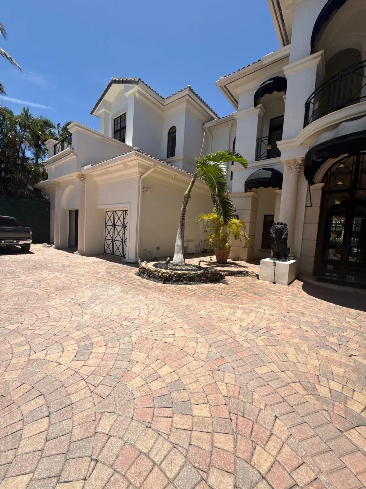 Exterior Painting in Boca Raton, Florida. Two-storey white stucco home exterior with tile roof, arched entry and dark trim, seen across a brick paver motor court.