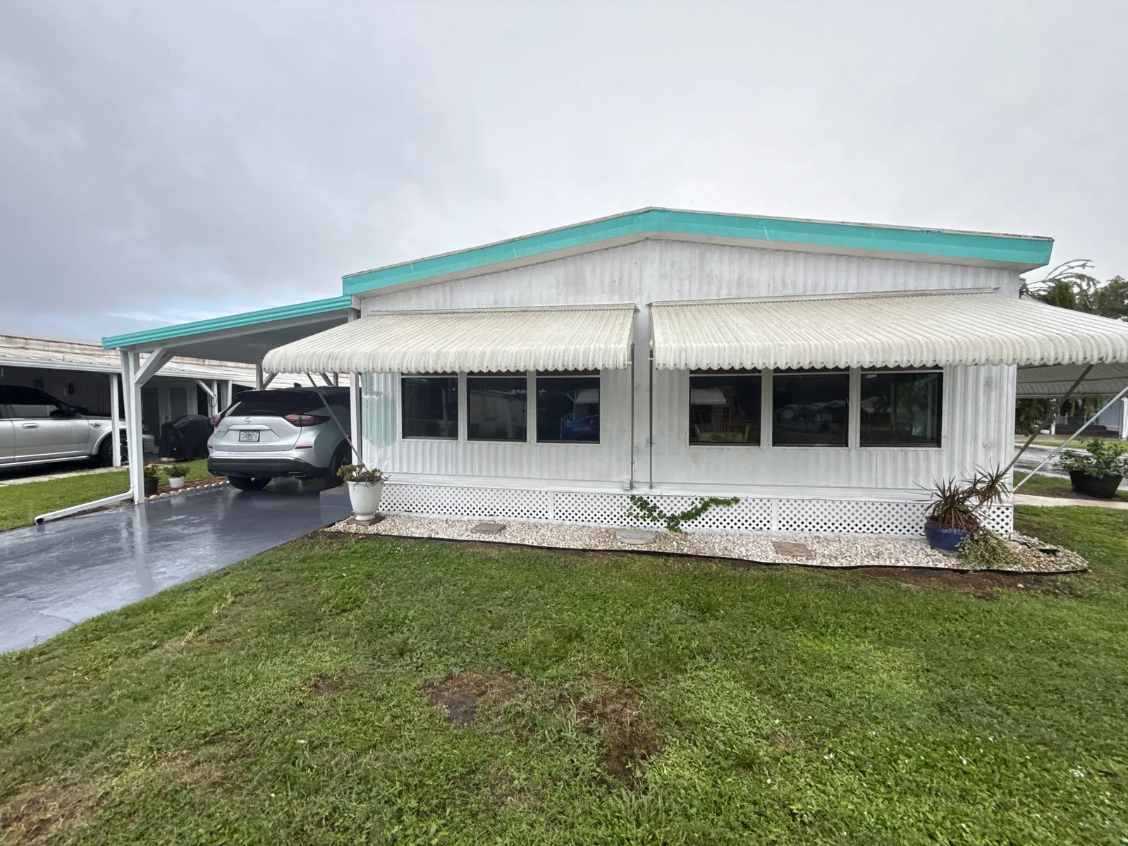 Exterior Painting in Coral Gardens, Florida. Corner view of a manufactured home with white metal siding, teal roofline trim, white window awnings and white lattice skirting.