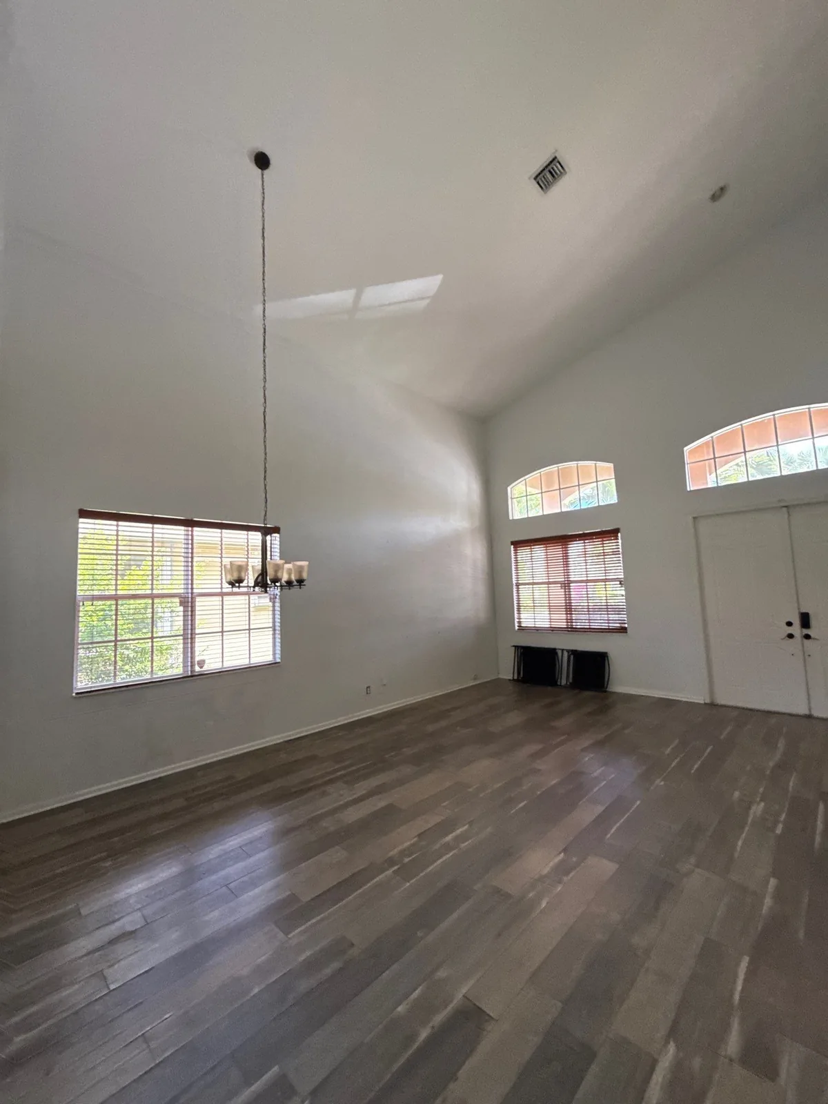 Interior Painting in Coral Gardens, Florida. Empty living room with white walls, vaulted ceiling, arched windows with blinds and dark wood floor.