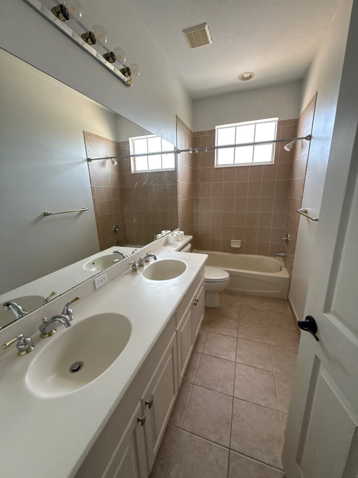 Interior Painting in Coral Gardens, Florida. Bathroom with white double-sink vanity, white painted walls and ceiling, glass-block window and tub-shower.