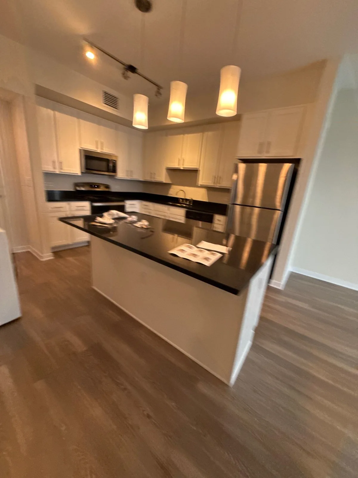 Interior Painting in Downtown Melbourne, Florida. Kitchen with white cabinets, dark stone countertops and island, stainless refrigerator, pendant and track lighting over wood-look flooring.