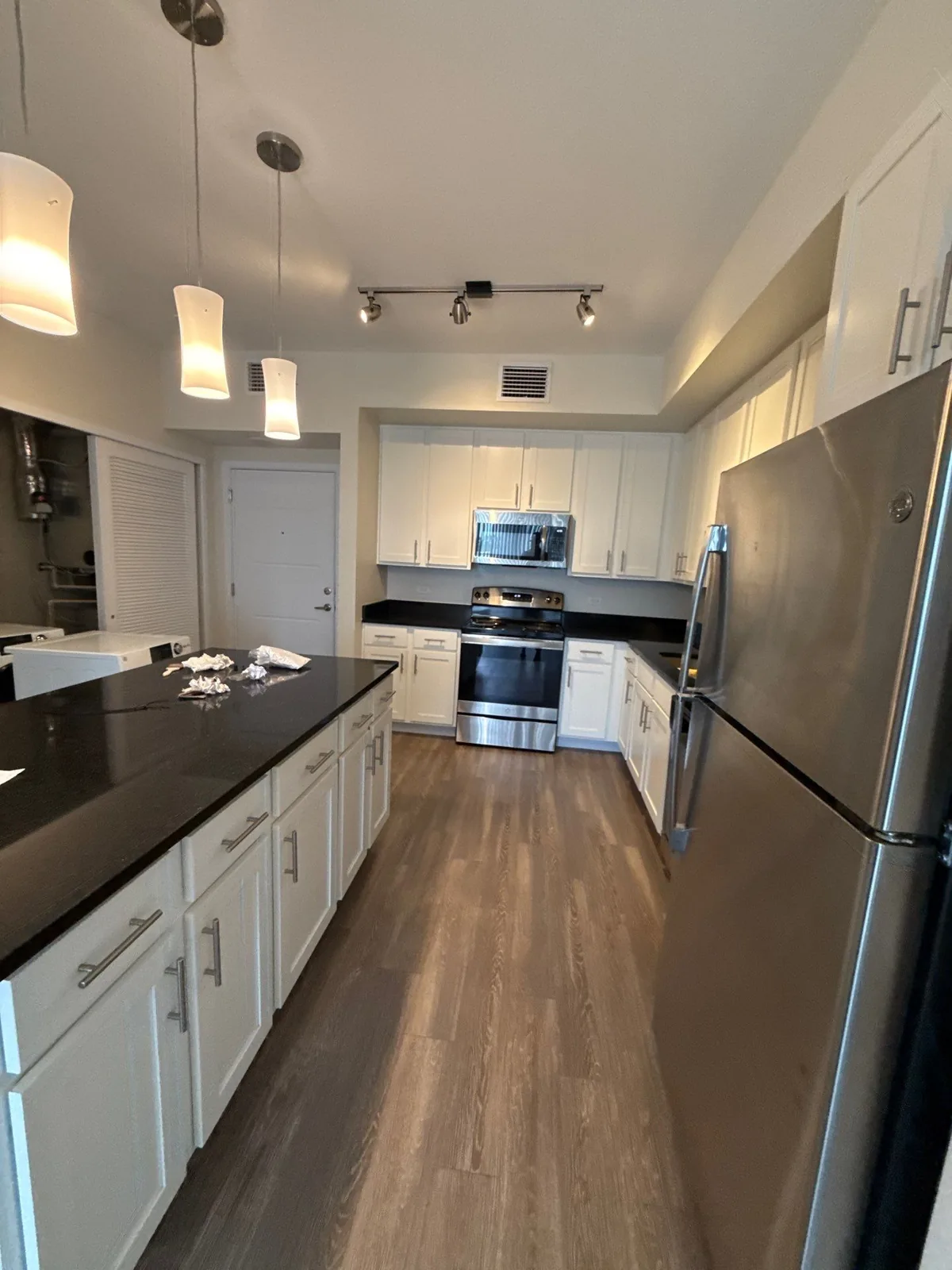 Interior Painting in Downtown Melbourne, Florida. Galley kitchen with white cabinets, dark countertops, stainless steel appliances, pendant and track lighting and wood-look flooring.