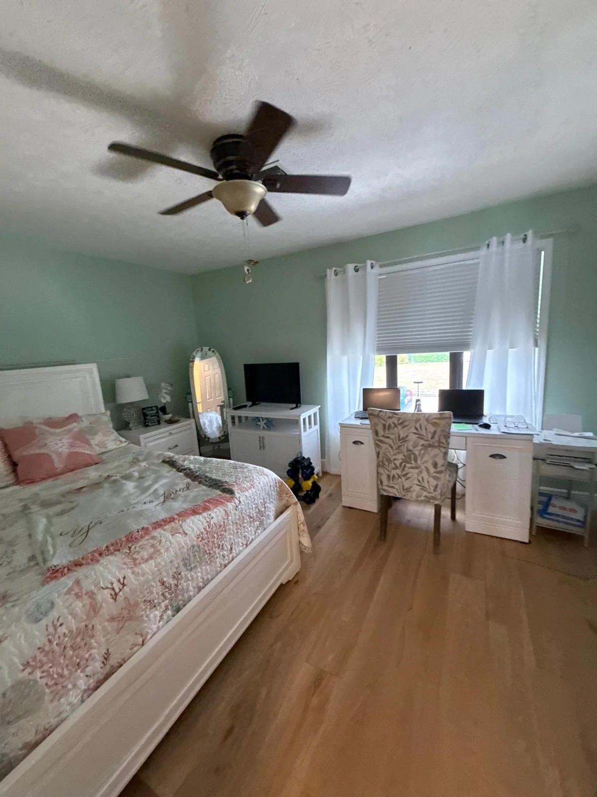 Interior Painting in Eden, Florida. Furnished bedroom with mint green painted walls, ceiling fan, wood flooring and a white desk under a curtained window.