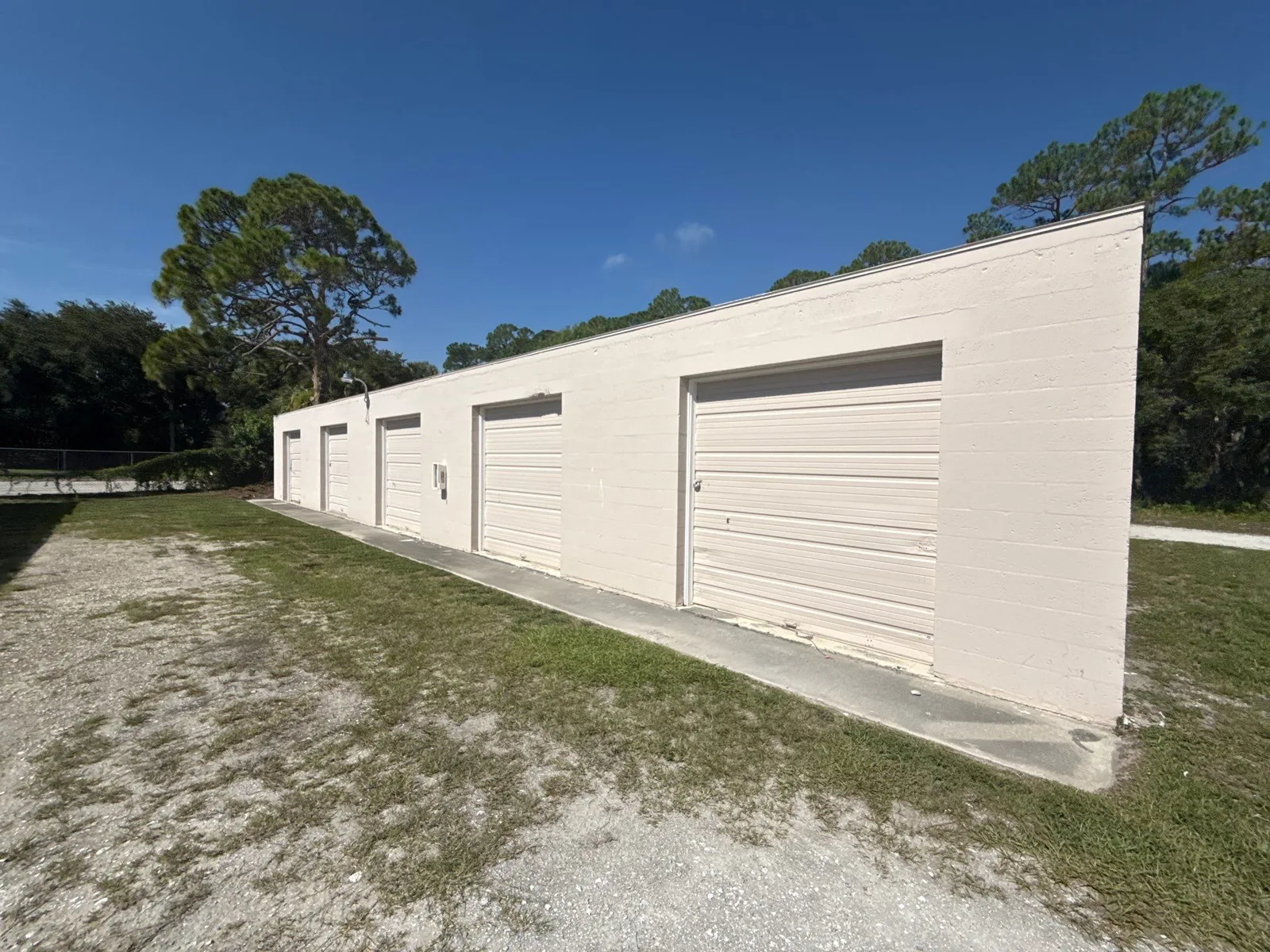 Commercial Painting in Florida Ridge, Florida. Single-storey concrete block building painted off-white, with four roll-up doors and a walk door, on a grass and gravel lot.