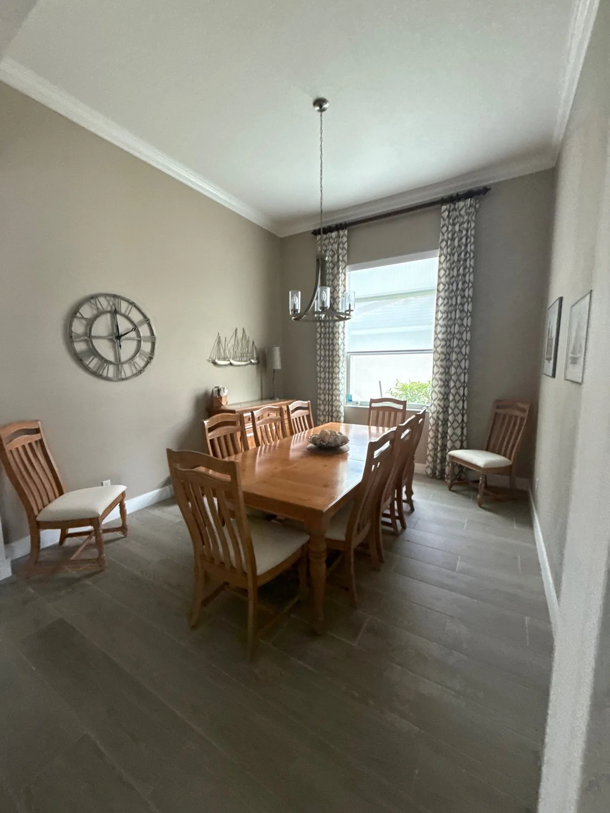 Interior Painting in Florida Ridge, Florida. Dining room with taupe walls, white crown moulding, wood table and eight chairs and a wall clock.