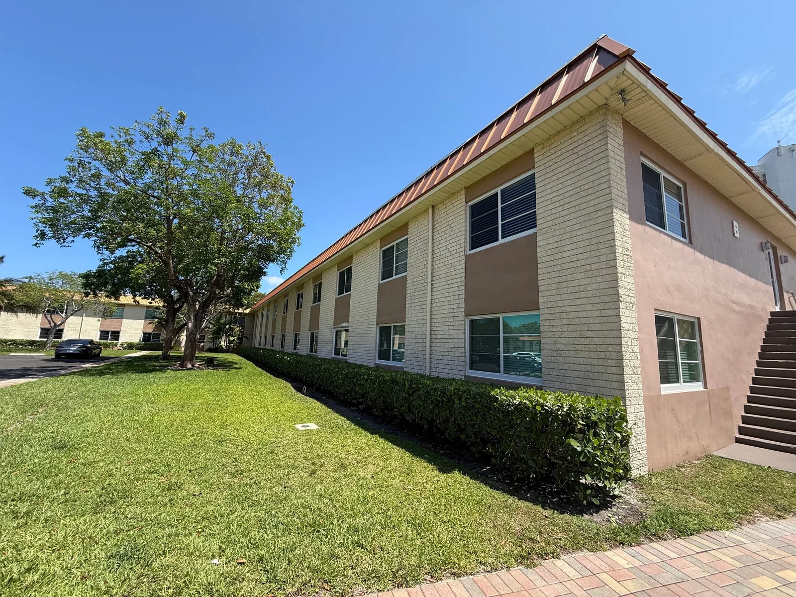 Commercial Painting in Fort Lauderdale, Florida. Corner of a two-storey building with painted block and stucco, hedge and lawn in front.