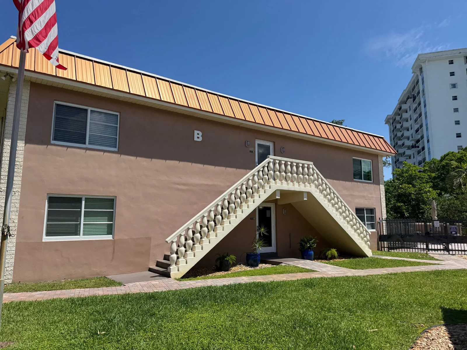Exterior Painting in Fort Lauderdale, Florida. Two-storey stucco apartment building painted mauve with a white balustrade exterior staircase and a ribbed metal roof.