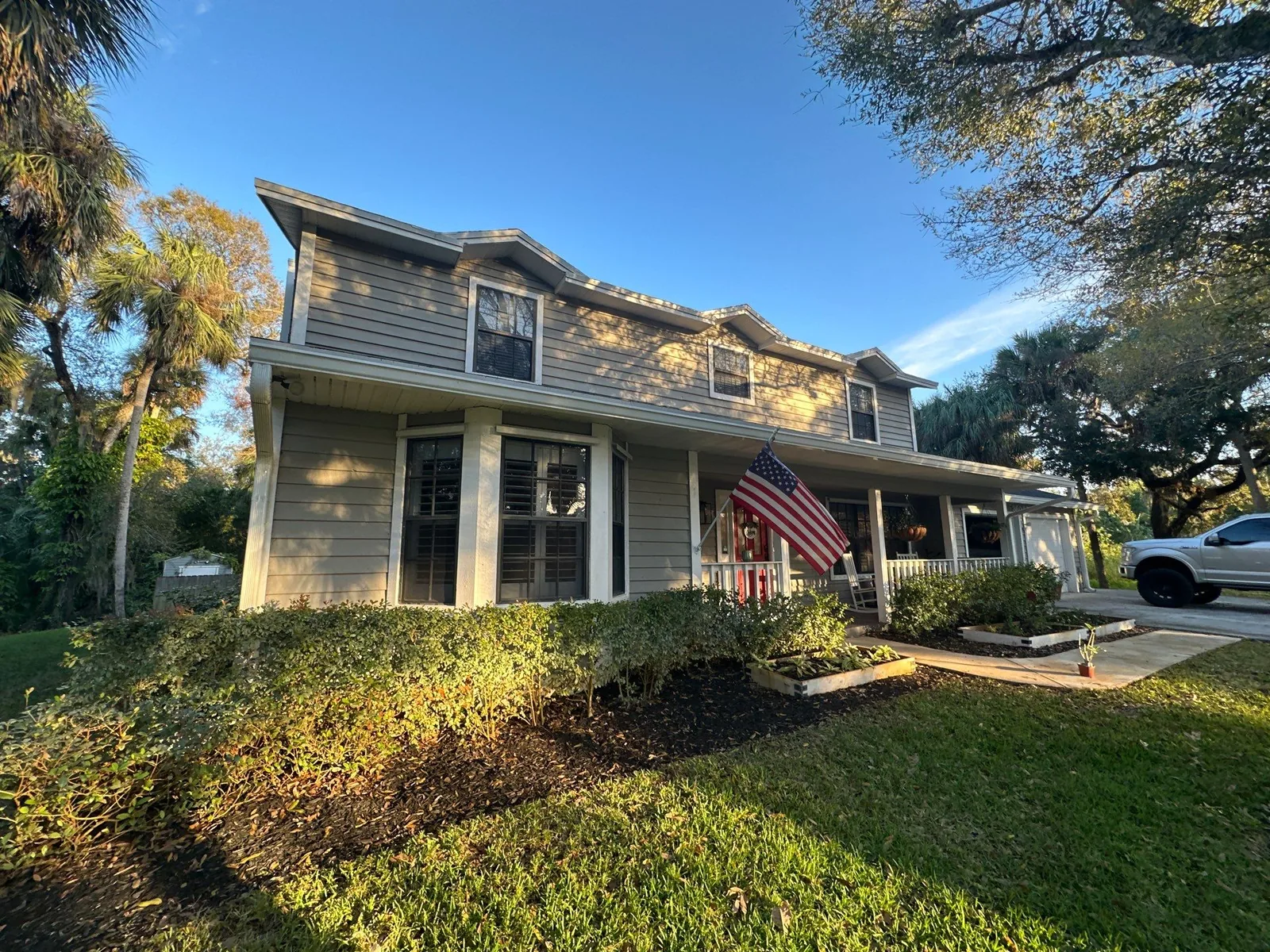 Exterior Painting in Fort Pierce, Florida. Front elevation of a two-storey house with lap siding, white trim and a covered front porch, with hedges and lawn in front.