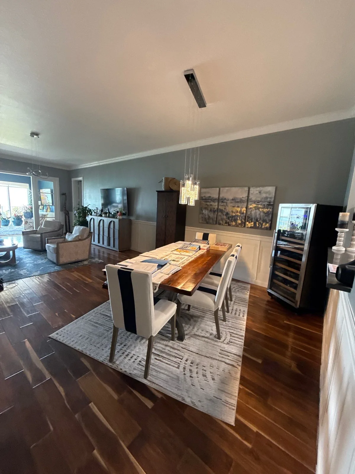 Interior Painting in Fort Pierce, Florida. Dining area with grey painted walls, dark hardwood flooring, wood table with white chairs and framed artwork.