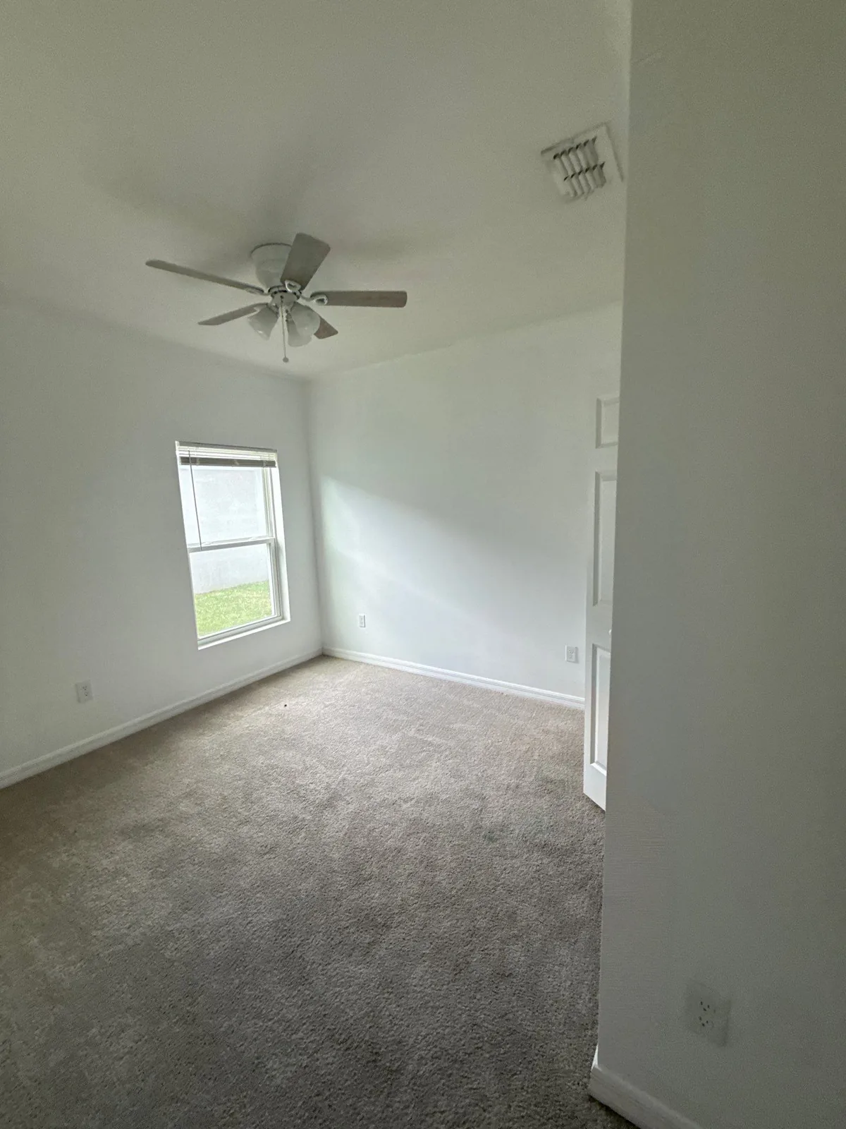 Interior Painting in Fort Pierce, Florida. Empty carpeted bedroom with freshly painted white walls and ceiling, ceiling fan and a window.