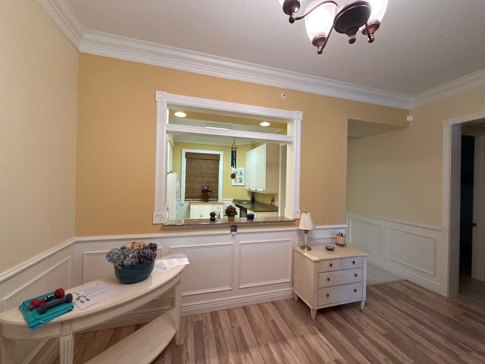 Interior Painting in Fort Pierce, Florida. Dining area with pale yellow upper walls, white wainscoting and chair rail, white crown molding and a framed pass-through mirror.