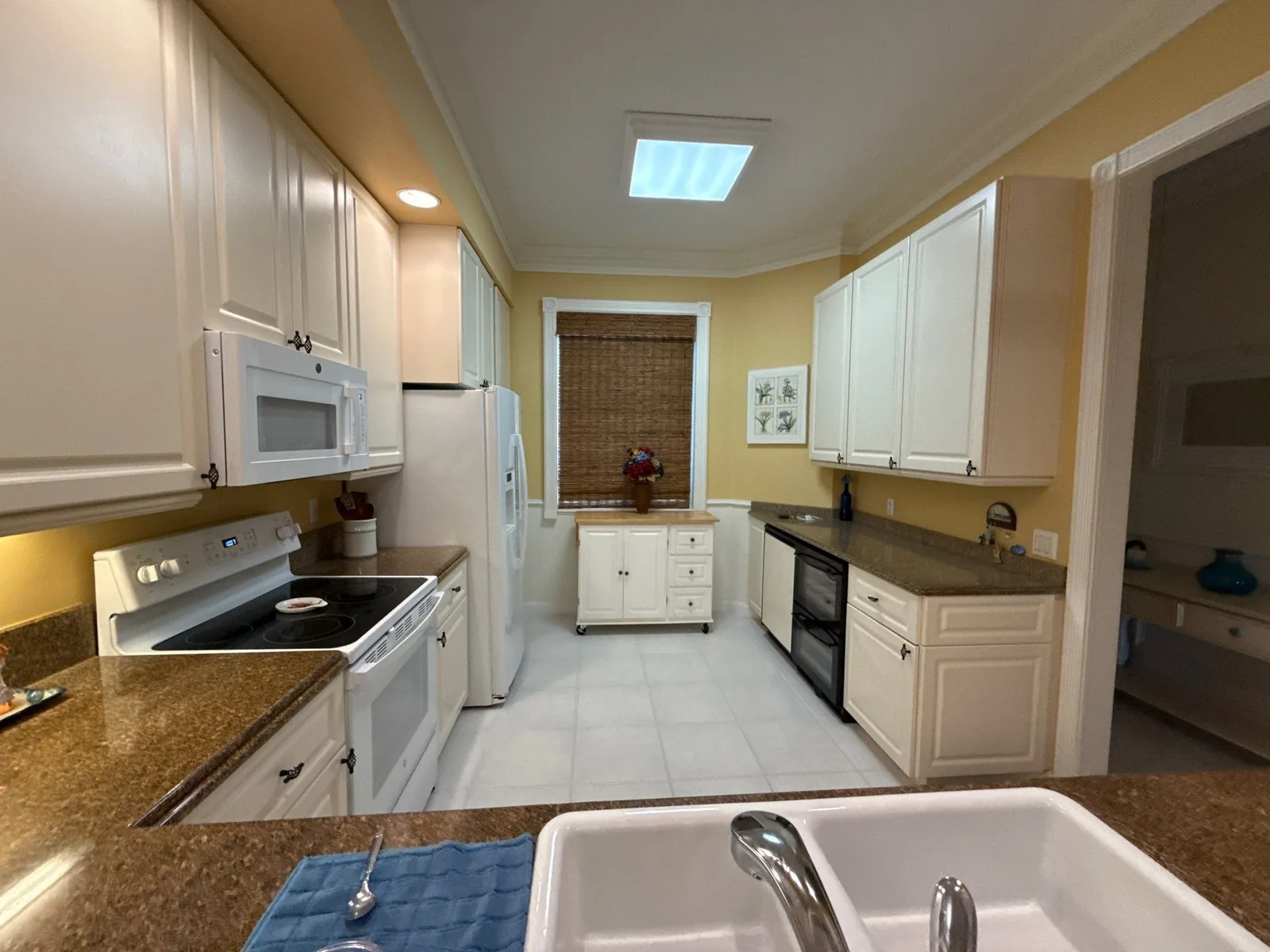 Interior Painting in Fort Pierce, Florida. Galley kitchen with white cabinets, pale yellow walls and white ceiling, viewed across a counter.