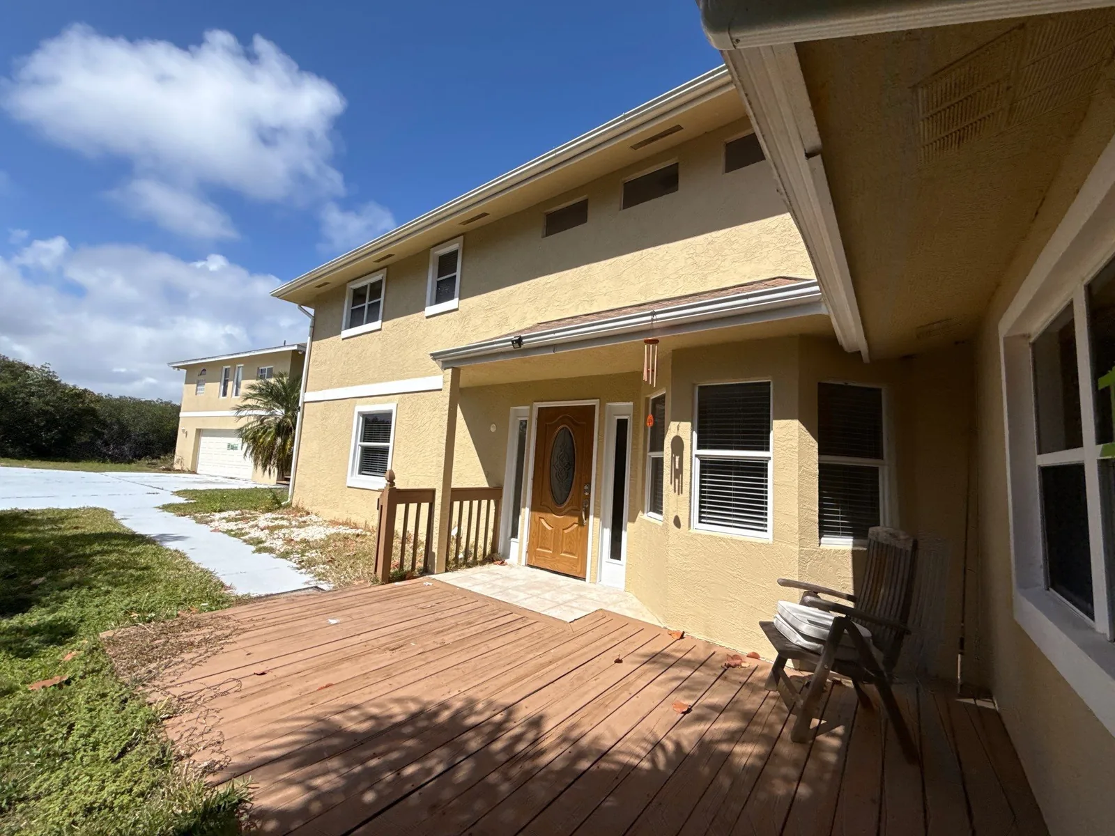 Exterior Painting in Gifford, Florida. Two-storey tan stucco house with white trim, a covered entry and a wooden deck across the front.