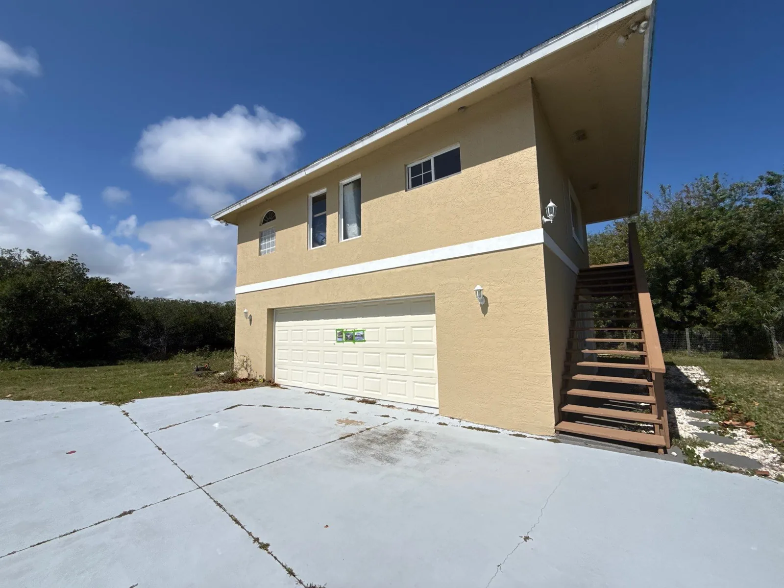 Exterior Painting in Gifford, Florida. Two-storey stucco house with attached garage, tan walls and white garage door, concrete driveway in foreground.