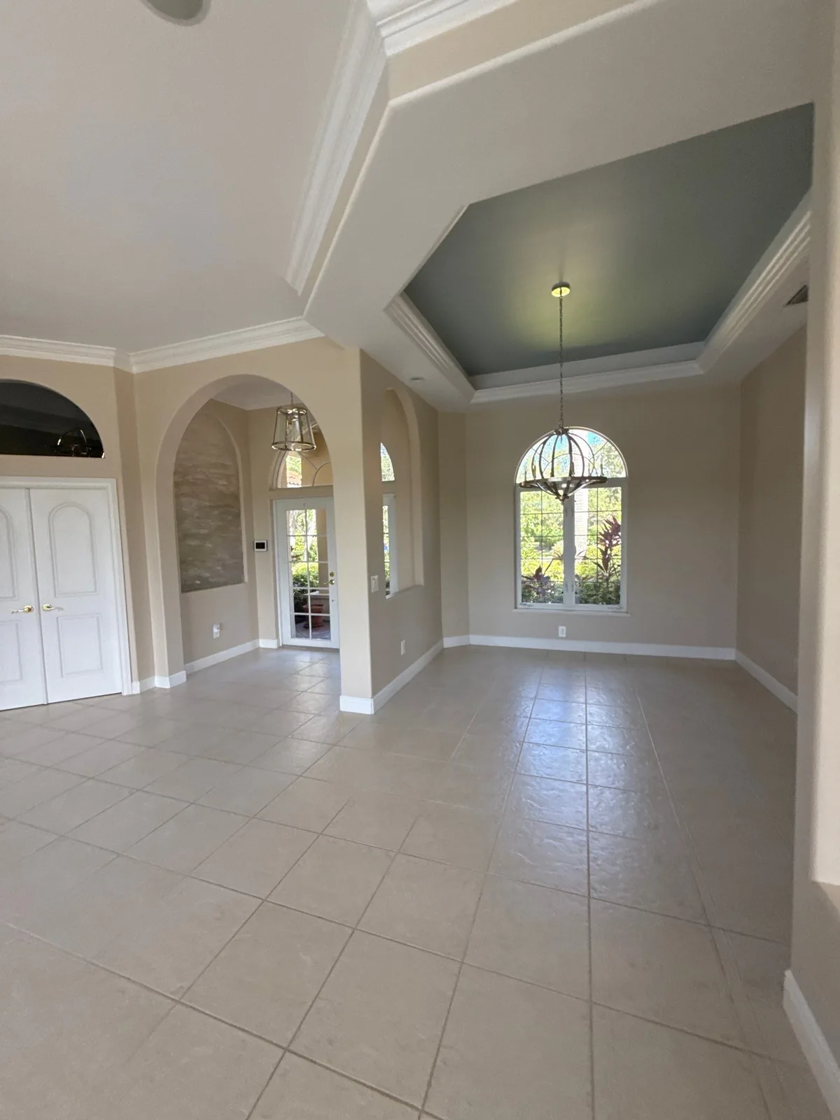 Interior Painting in Gifford, Florida. Empty foyer and dining area with beige walls, white crown moulding, a blue-green tray ceiling and arched transom windows.