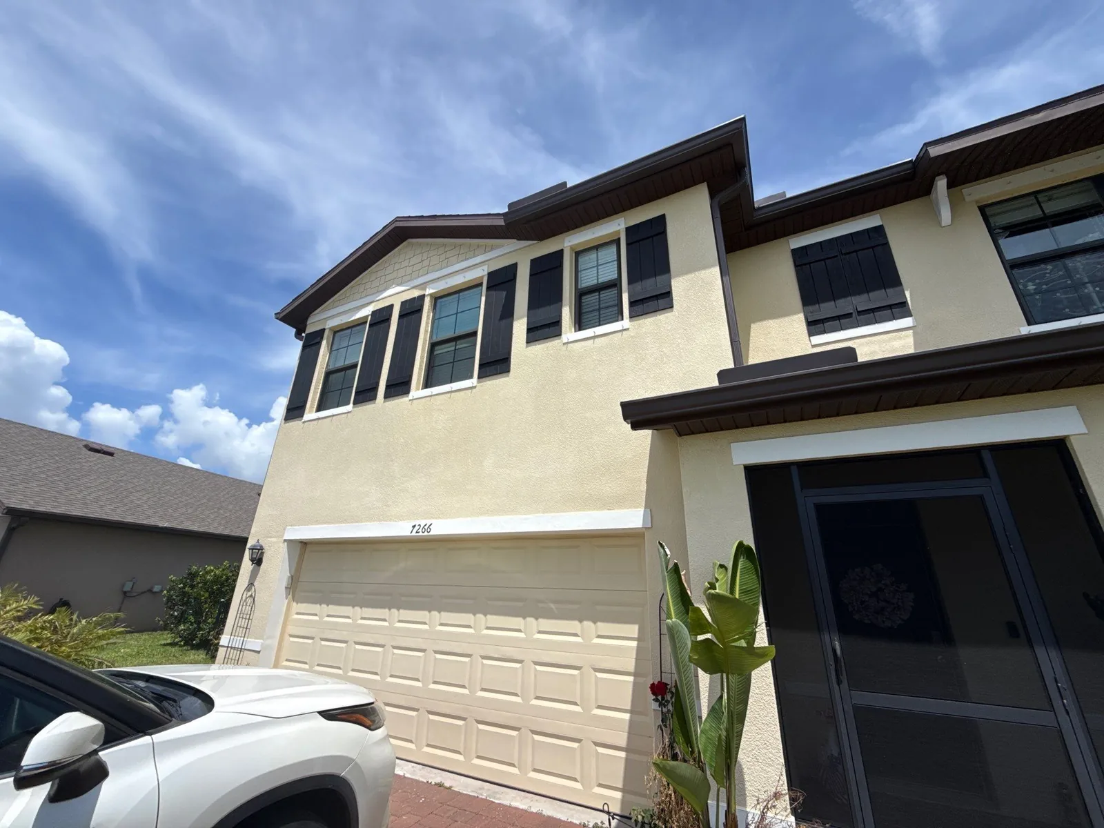 Exterior Painting in Grant-Valkaria, Florida. Two-storey stucco townhouse exterior, tan walls with darker trim and shutters, white garage door, under a clear blue sky.