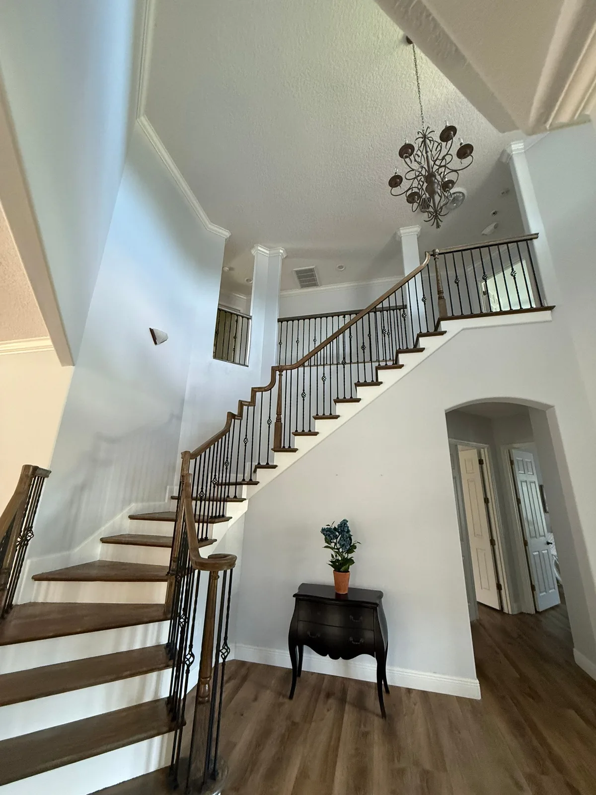Interior Painting in Grant-Valkaria, Florida. Two-storey entry foyer with a curved staircase, white walls and trim, wood treads and handrail with dark metal balusters, and a hanging chandelier.