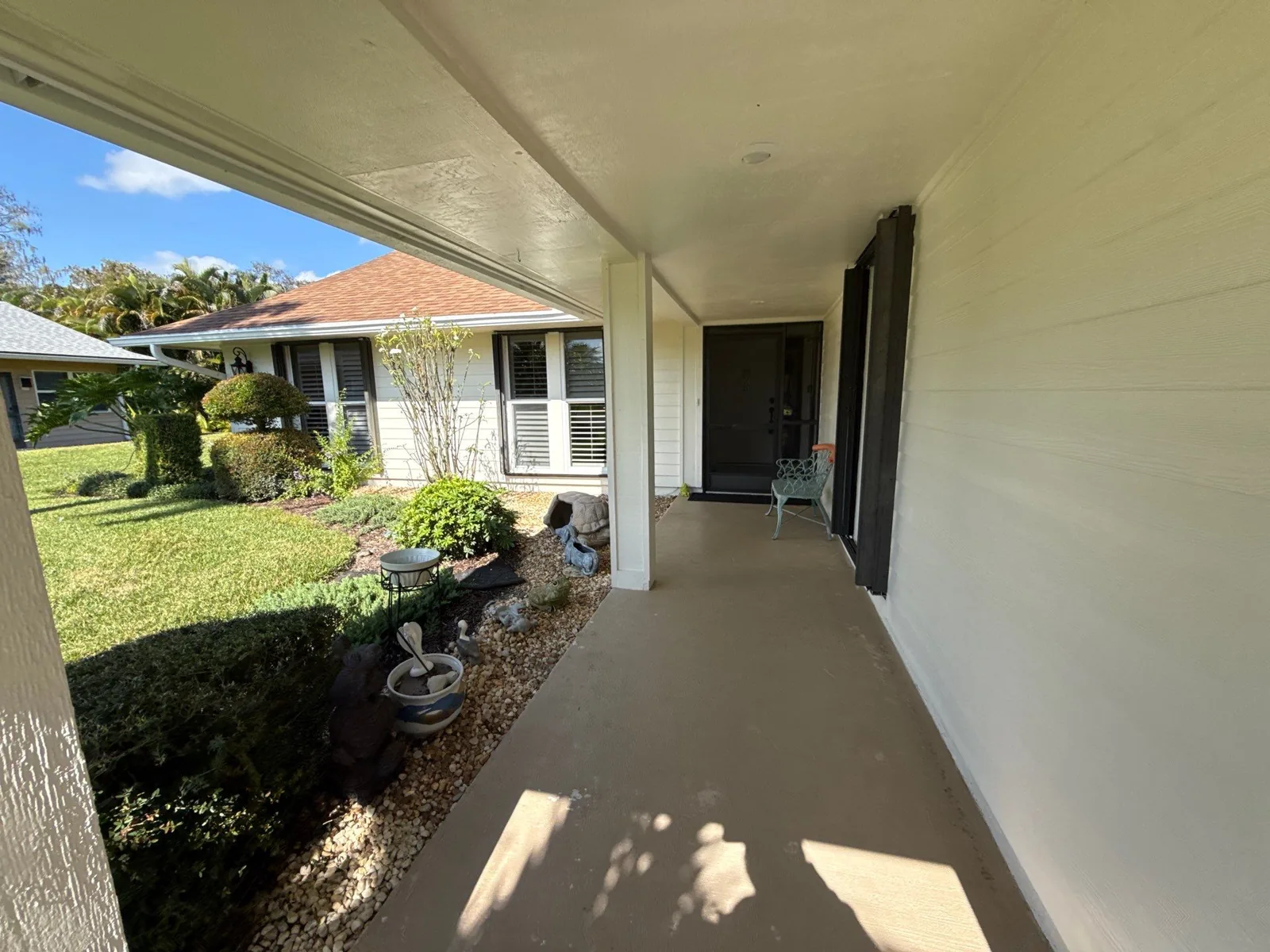Exterior Painting in Hobe Sound, Florida. Covered front entry walkway of a single-storey home, cream painted walls and soffit with a dark front door.