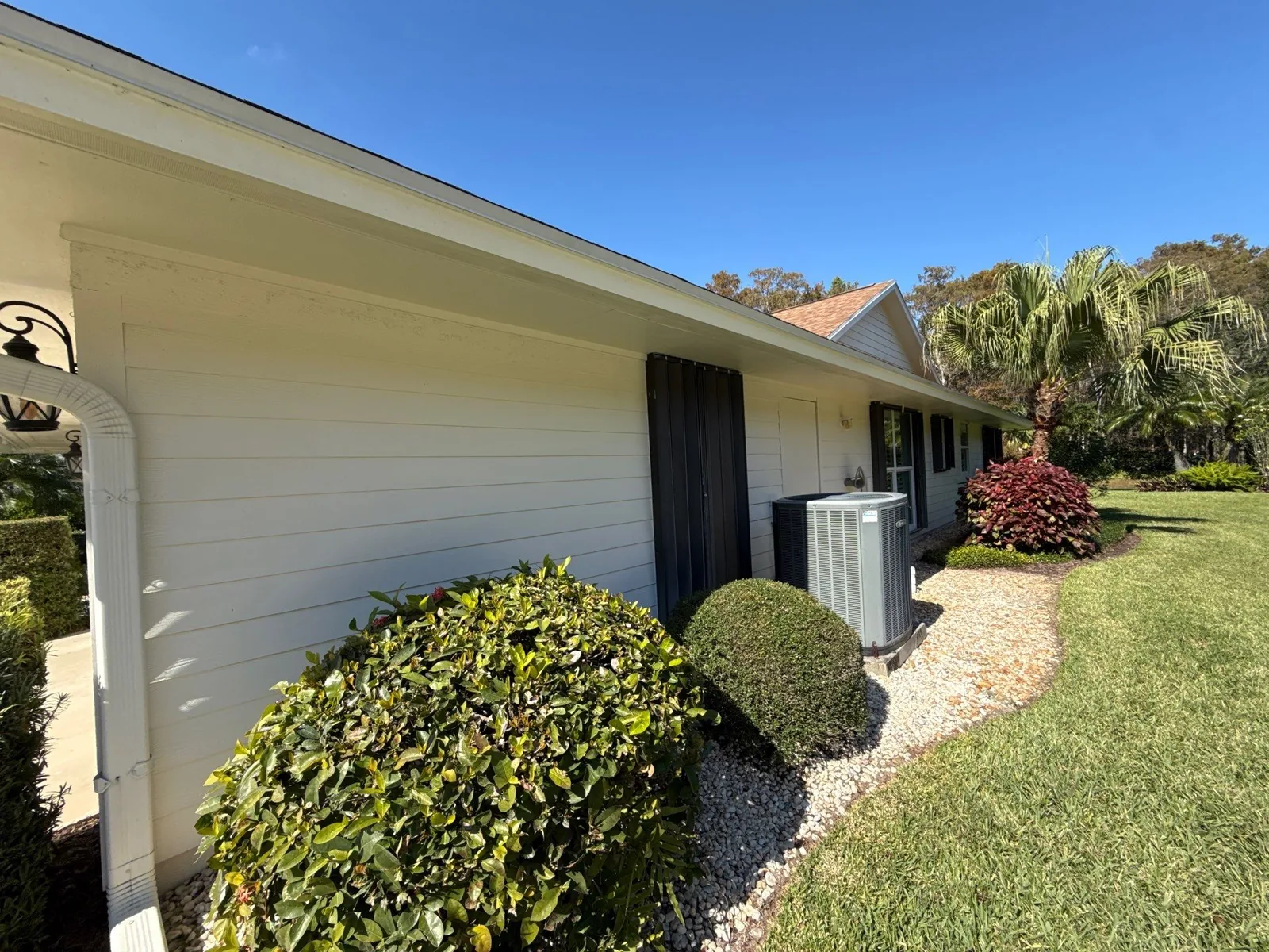 Exterior Painting in Hobe Sound, Florida. Side elevation of a single-storey home with white horizontal siding and trimmed hedges.
