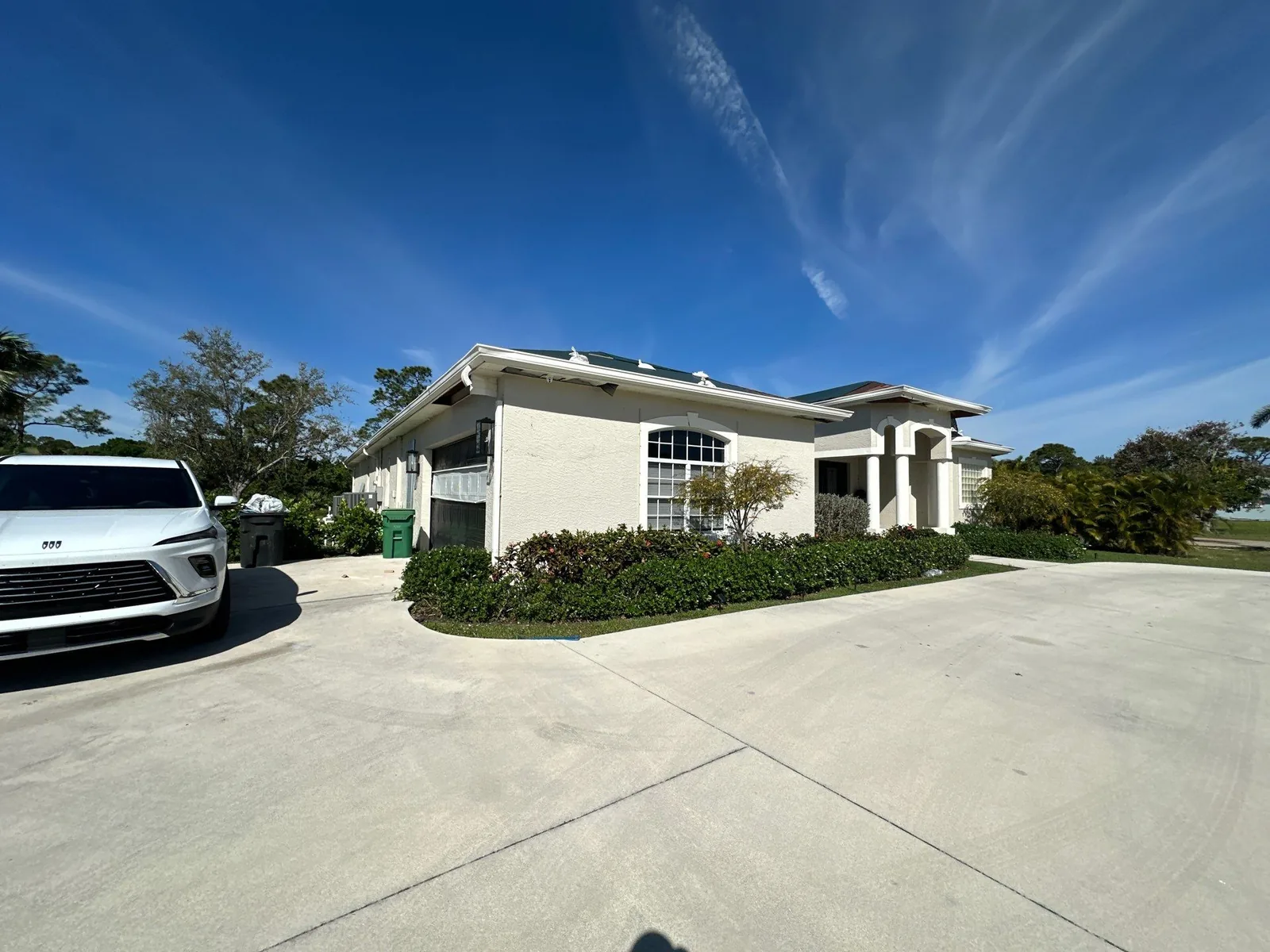 Exterior Painting in Indian River Estates, Florida. Single-storey stucco building with white walls, tile roof and arched entry under a blue sky.