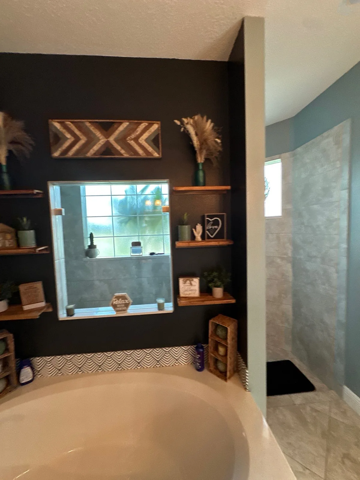 Interior Painting in Indian River Estates, Florida. Bathroom with dark charcoal accent wall, wood floating shelves and a white soaking tub beside a tiled shower.
