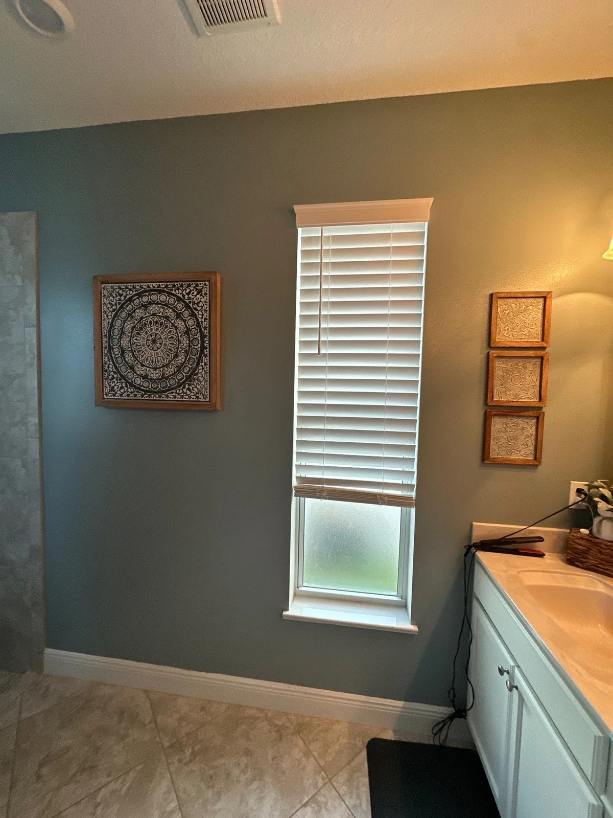 Interior Painting in Indian River Estates, Florida. Bathroom wall painted muted blue-green with white window trim, blinds and white baseboard beside a vanity.