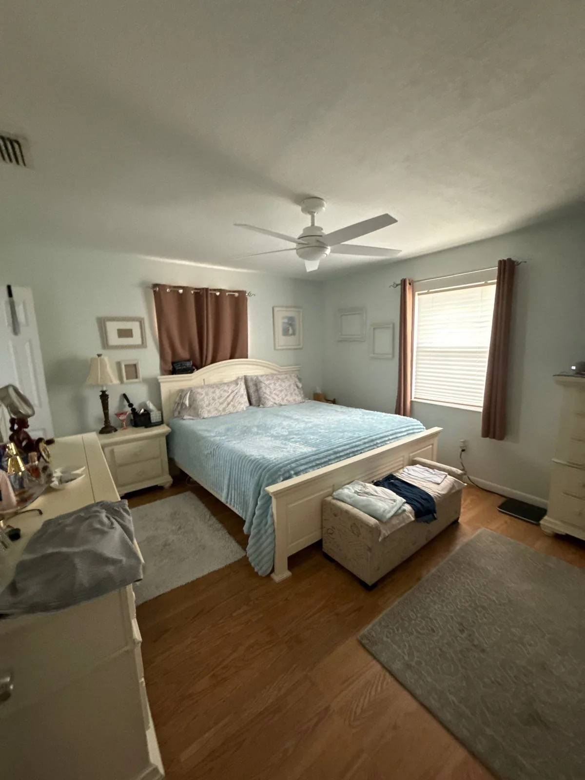 Interior Painting in Indian River Estates, Florida. Furnished bedroom with pale painted walls and ceiling, ceiling fan and wood-look flooring.