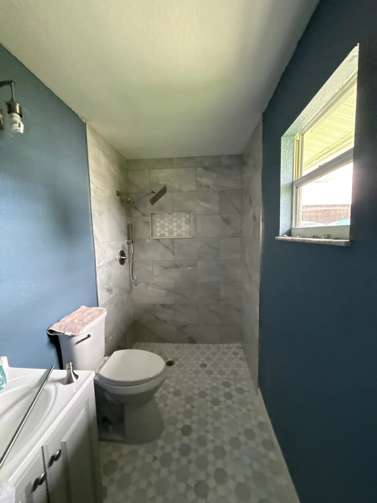Interior Painting in Indian River Estates, Florida. Bathroom with dark blue painted walls and white ceiling, tiled walk-in shower and vanity.
