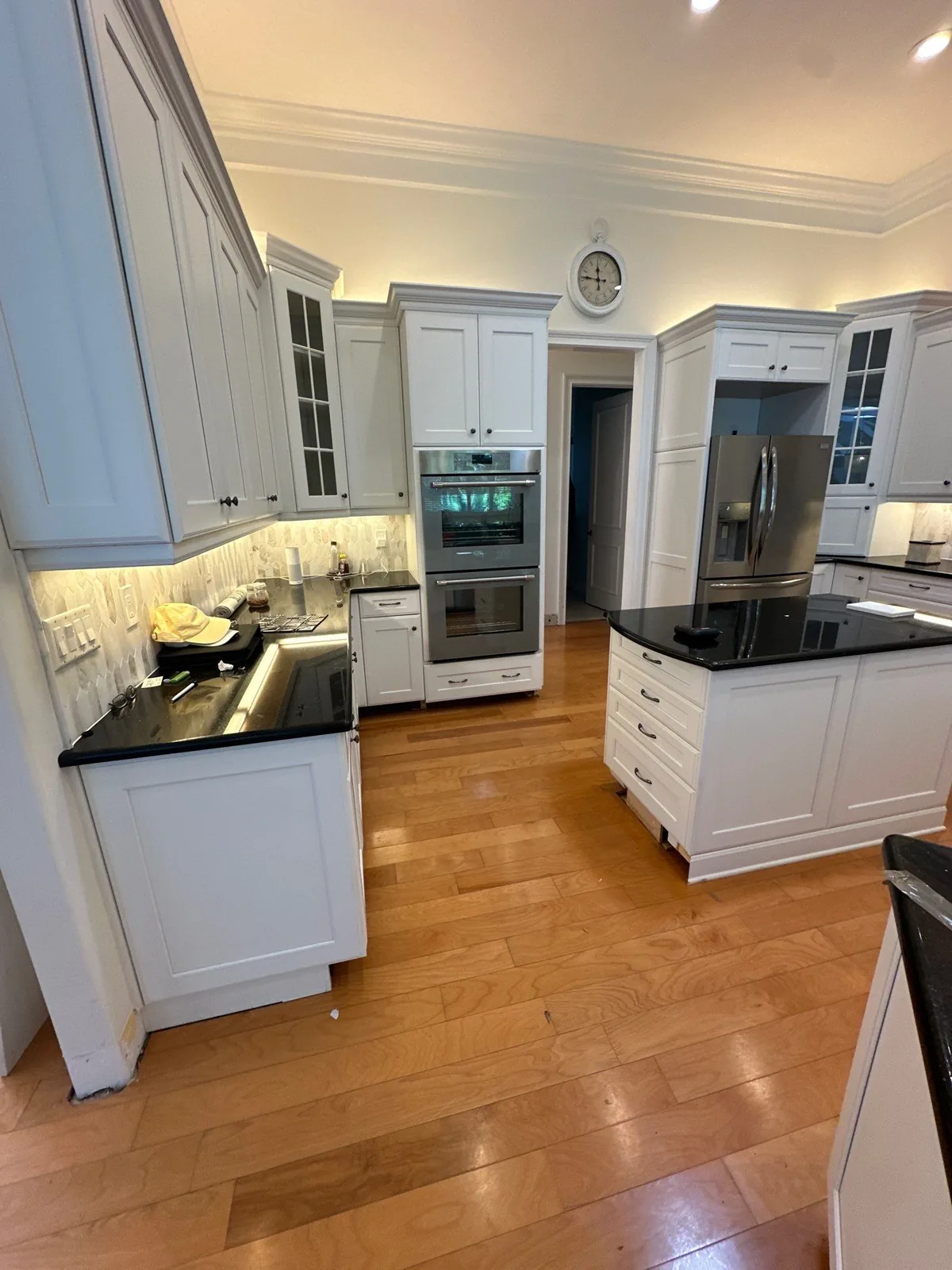 Cabinet Refinishing in Indian River Shores, Florida. Kitchen with white cabinetry, dark granite countertops, stainless double wall ovens and refrigerator, and a matching island on wood flooring.
