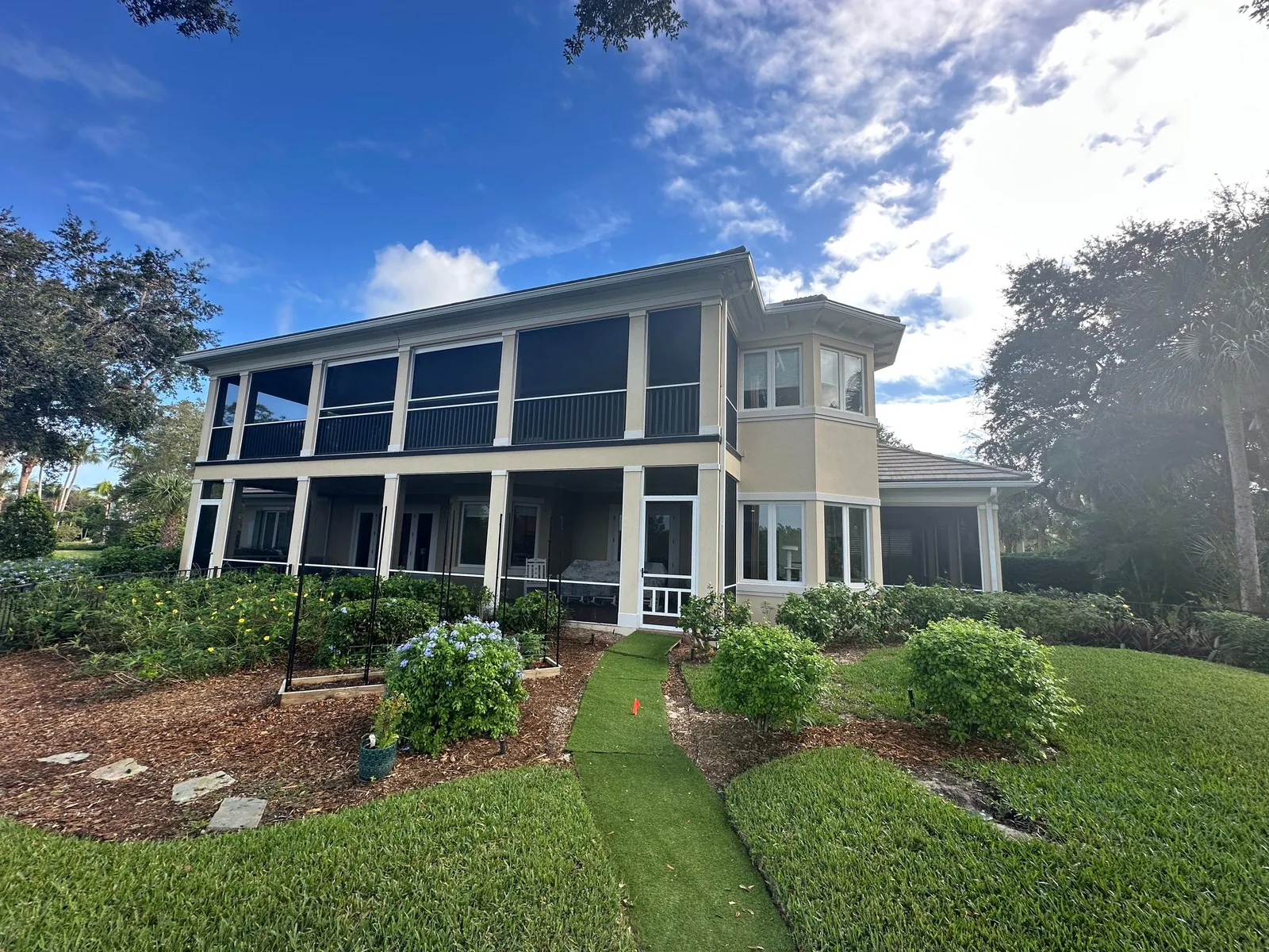 Exterior Painting in Indian River Shores, Florida. Two-storey house exterior with white and beige walls, screened porches on both levels, lawn and landscaping.