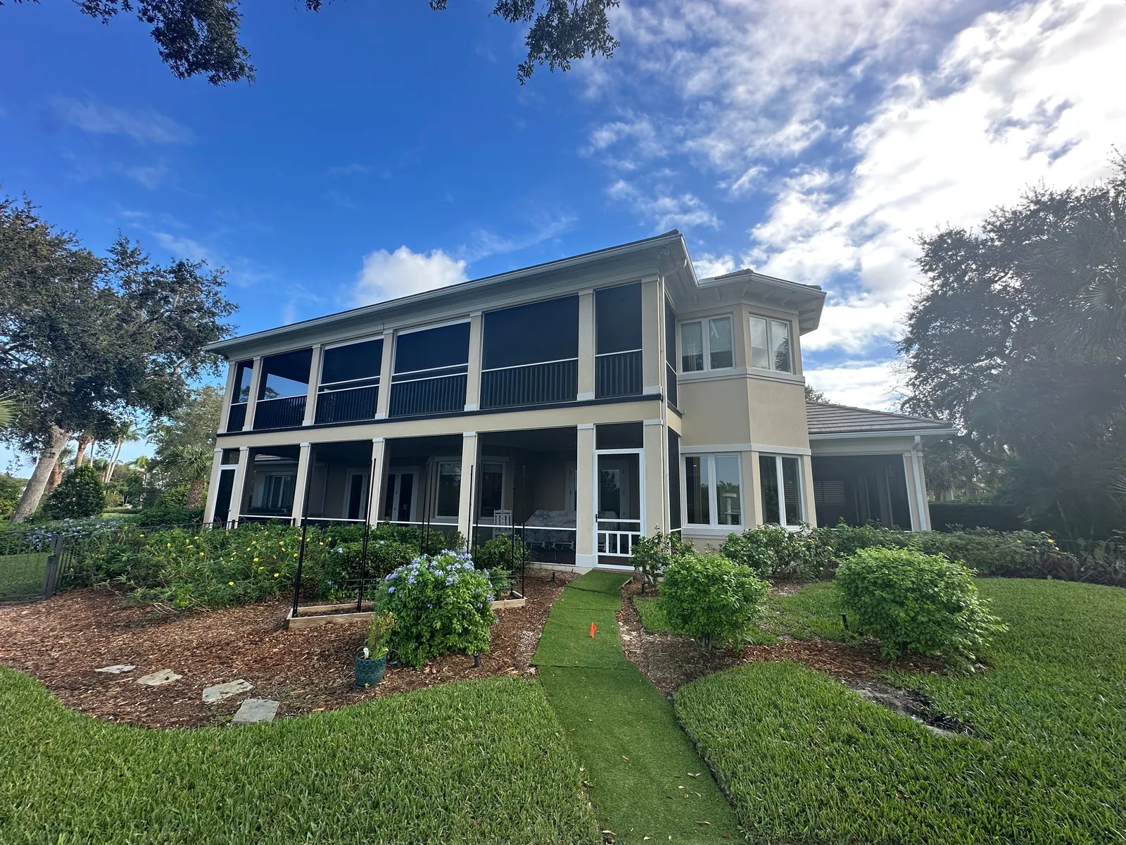 Exterior Painting in Indian River Shores, Florida. Two-storey house exterior with screened upper and lower porches, painted trim, lawn and shrub beds.