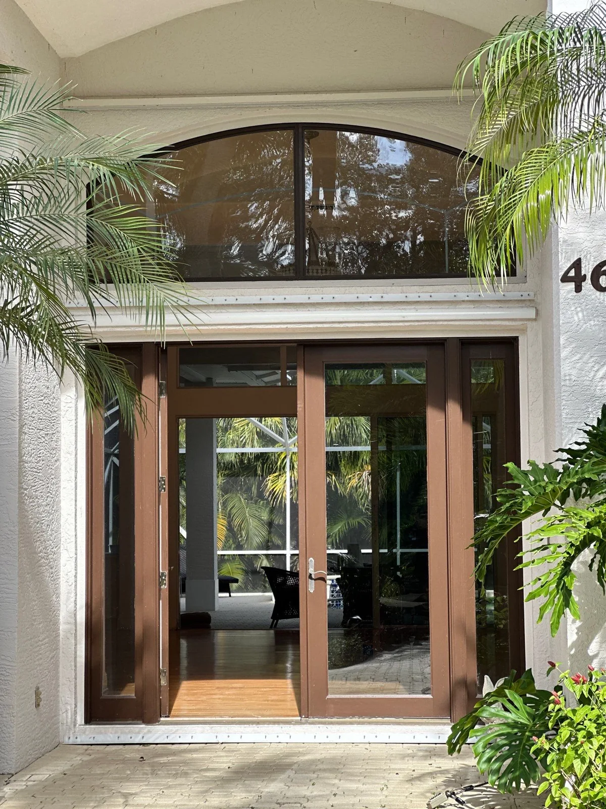 Exterior Painting in Indian River Shores, Florida. Front entry of a white stucco home with a dark wood-framed glass double door, arched transom window and palms on either side.