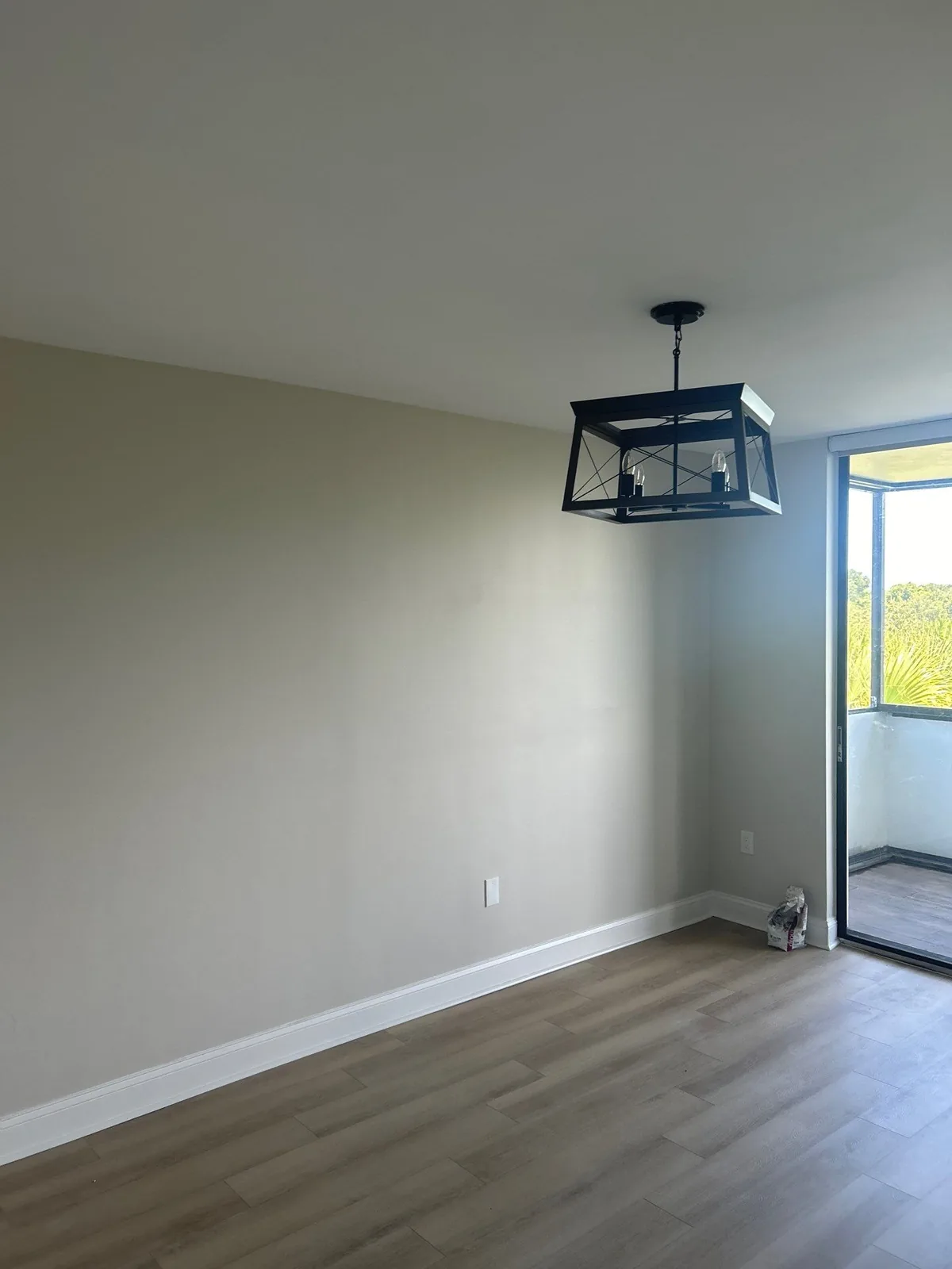 Interior Painting in Indian River Shores, Florida. Empty room with freshly painted walls, white baseboards, wood-look flooring, a lantern pendant light and a sliding glass door.