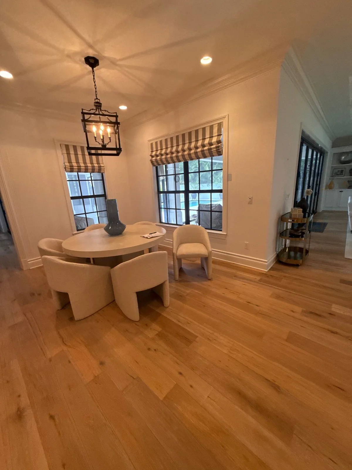 Interior Painting in Indian River Shores, Florida. Dining area with white painted walls and trim, lantern pendant over a round table, roman shades and wood floor.