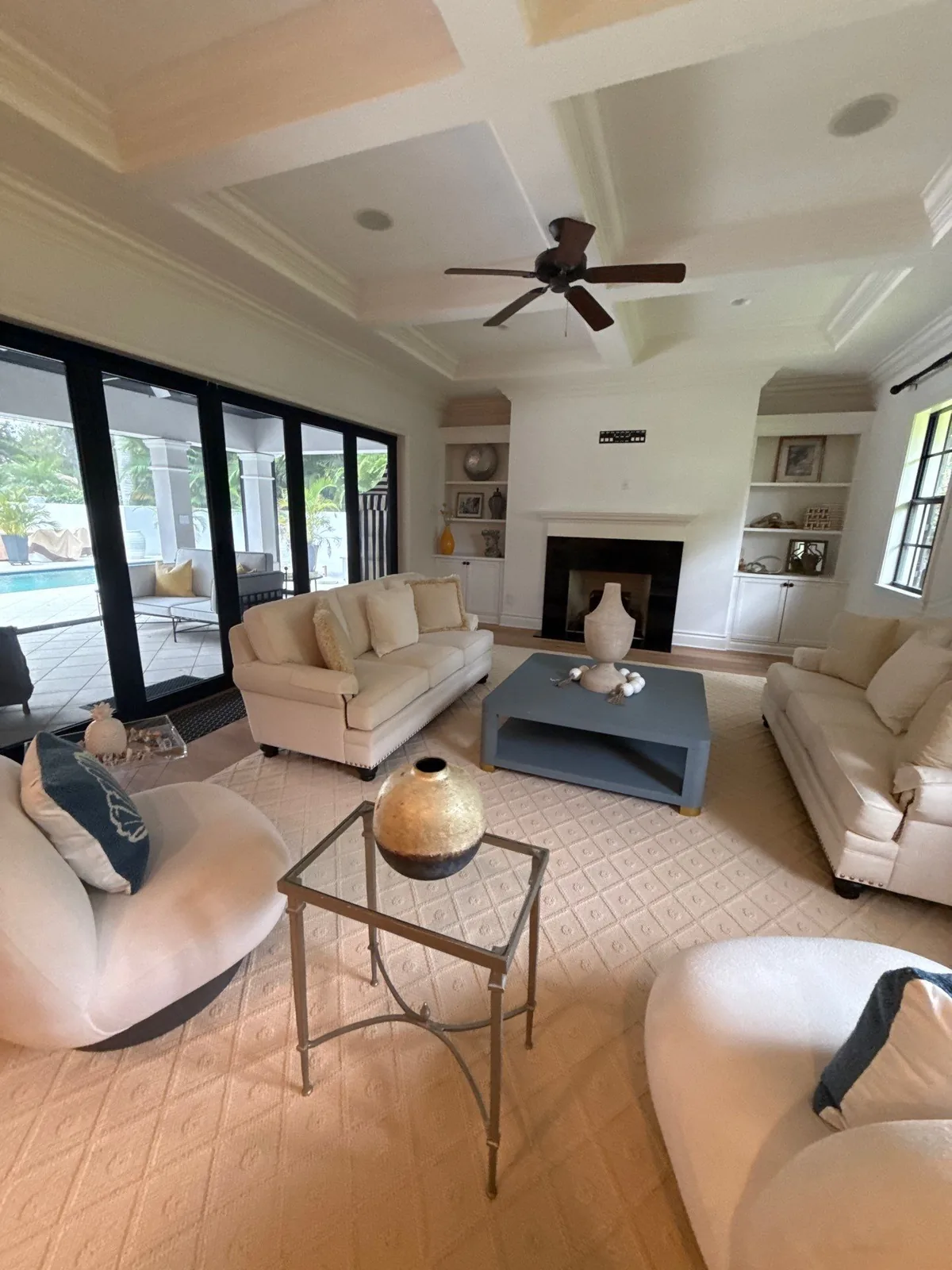 Interior Painting in Indian River Shores, Florida. Living room with white painted walls and coffered ceiling, fireplace with built-in niches, sofas and sliding doors to a pool.