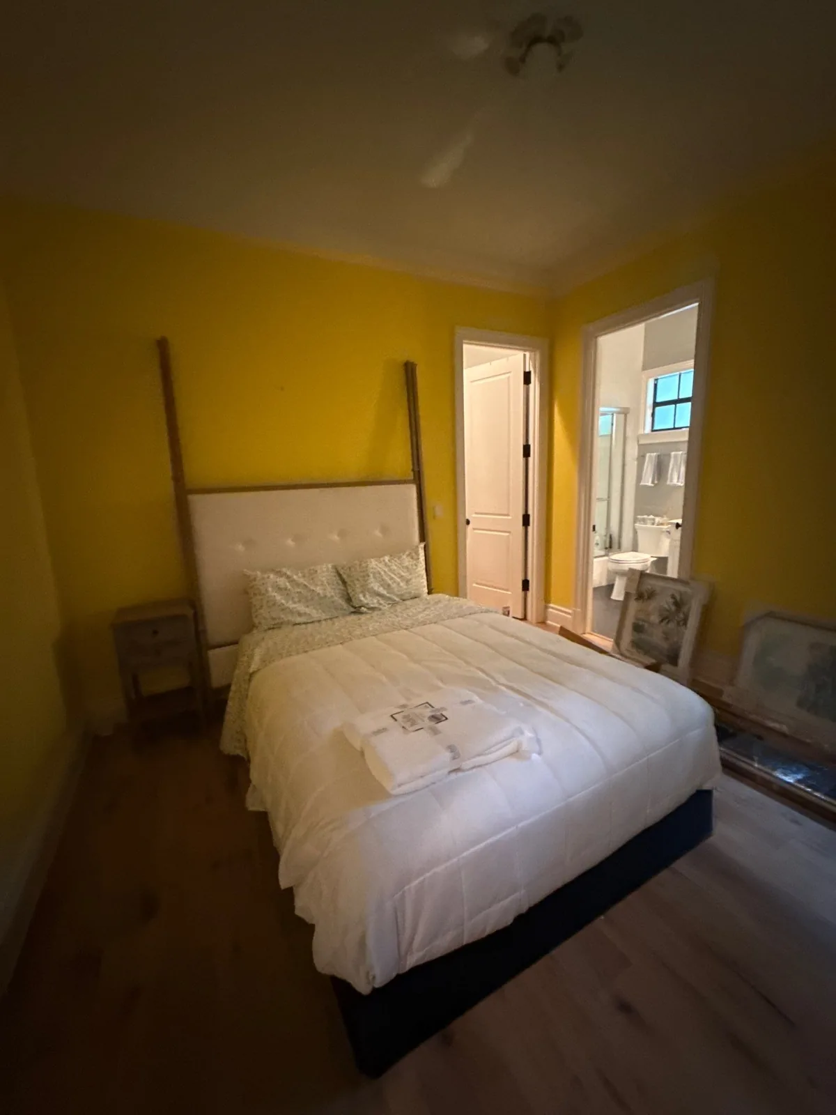 Interior Painting in Indian River Shores, Florida. Bedroom with yellow painted walls and white trim, made bed with white bedding and wood flooring.