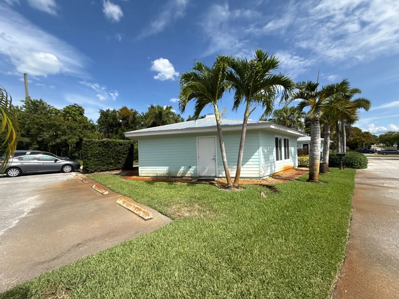 Commercial Painting in Jensen Beach, Florida. Single-storey building with pale green horizontal siding and white fascia, palm trees and an adjacent parking lot.