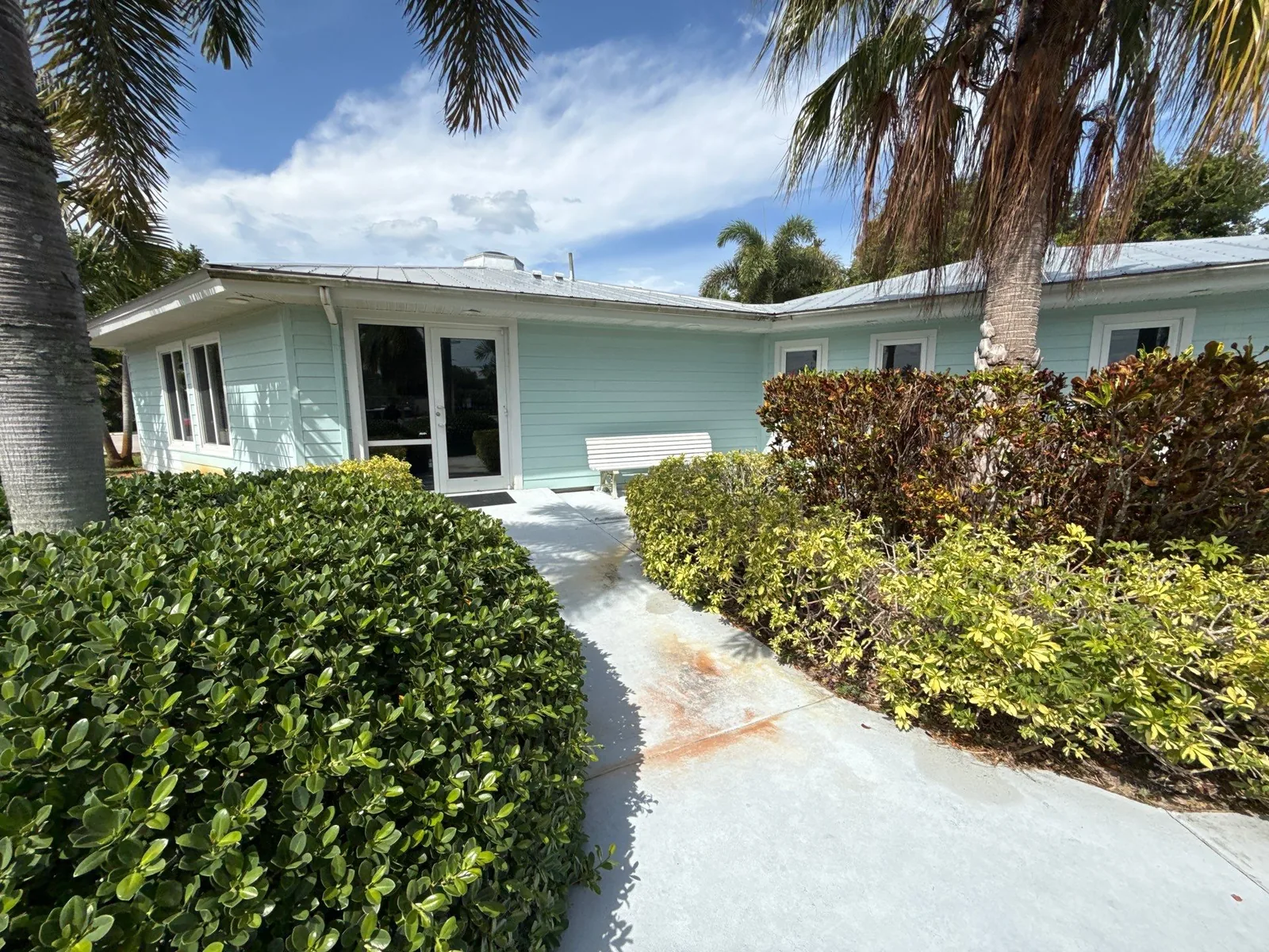 Exterior Painting in Jensen Beach, Florida. Single-storey home with light aqua horizontal siding and white trim, concrete walkway and trimmed hedges in front.