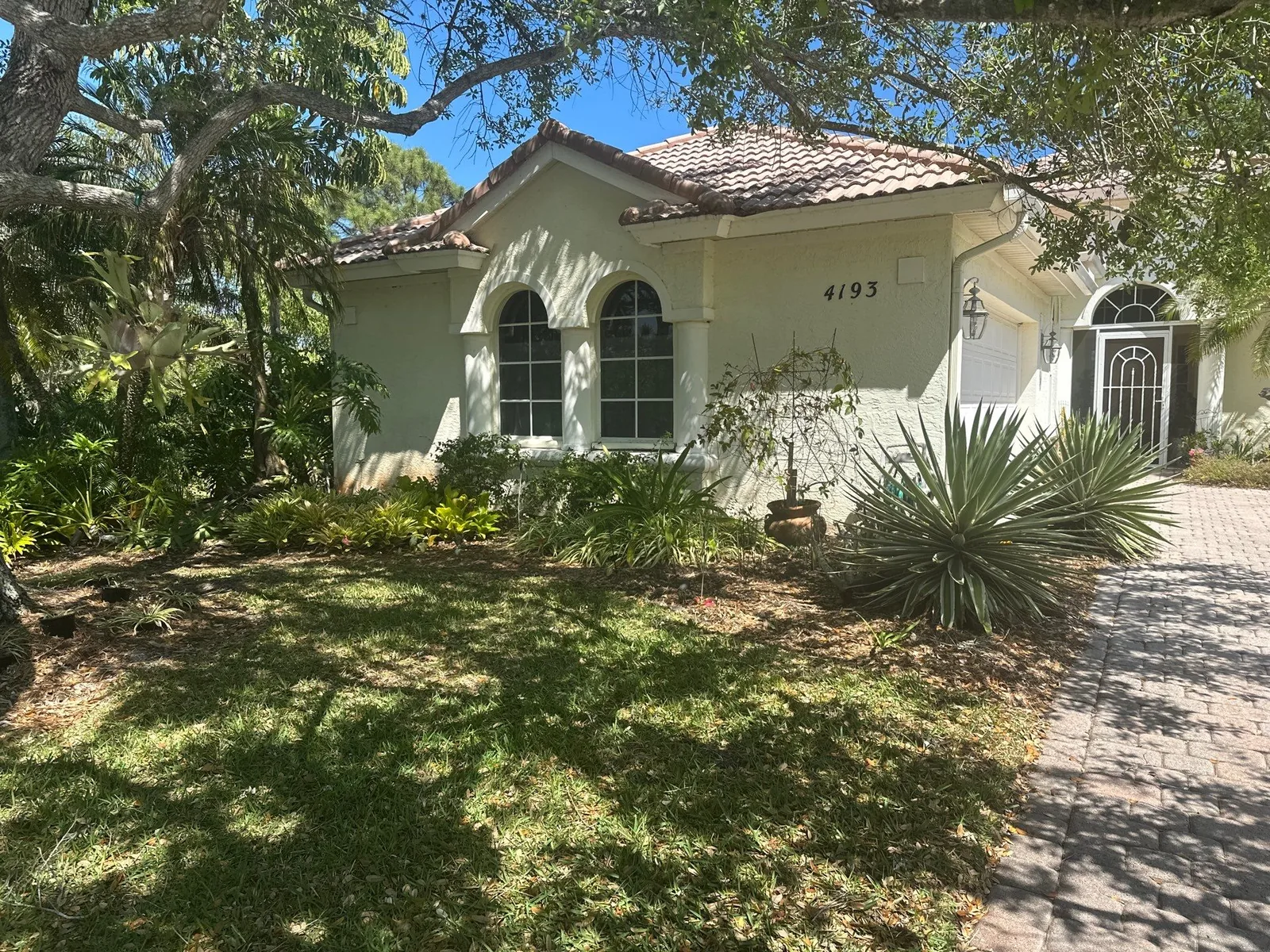 Exterior Painting in Jensen Beach, Florida. Single-storey stucco home exterior, pale green walls with white trim and arched windows, barrel tile roof.