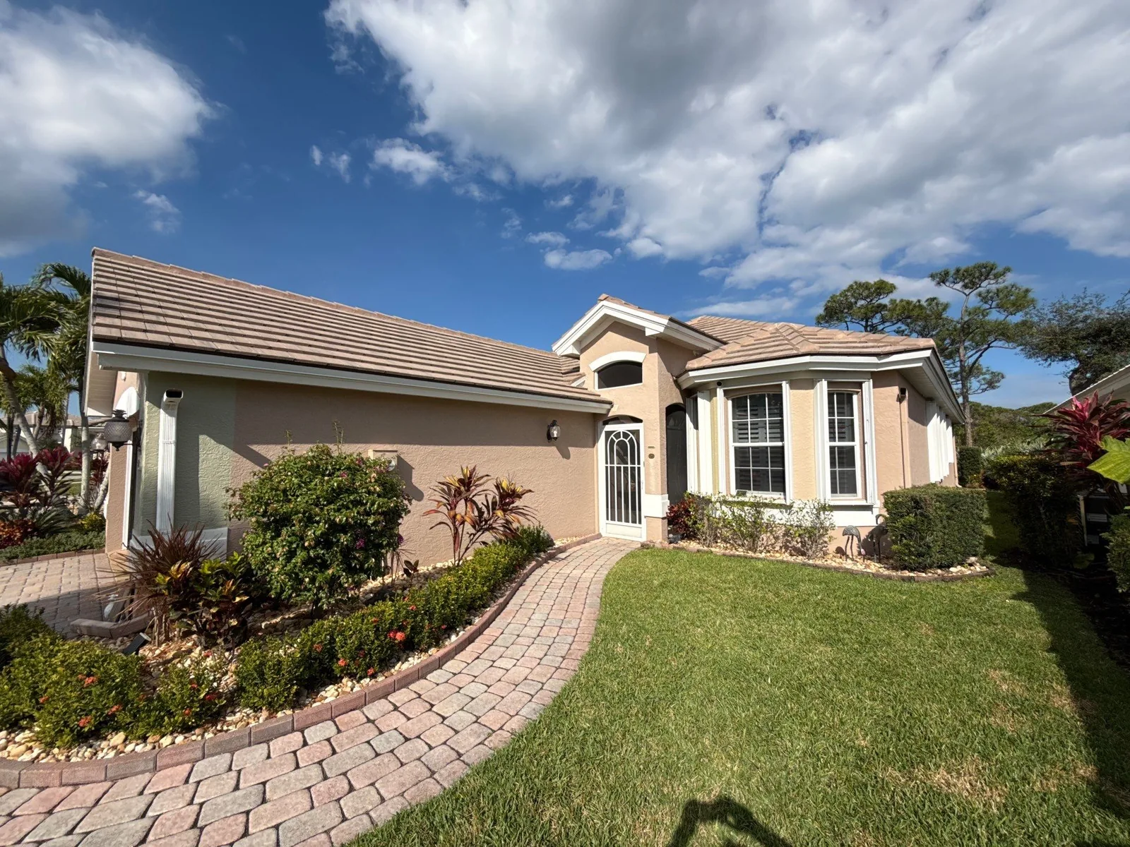 Exterior Painting in Jensen Beach, Florida. Single-storey house exterior in salmon stucco with white trim and garage door, tile roof, paver walkway and landscaped beds.