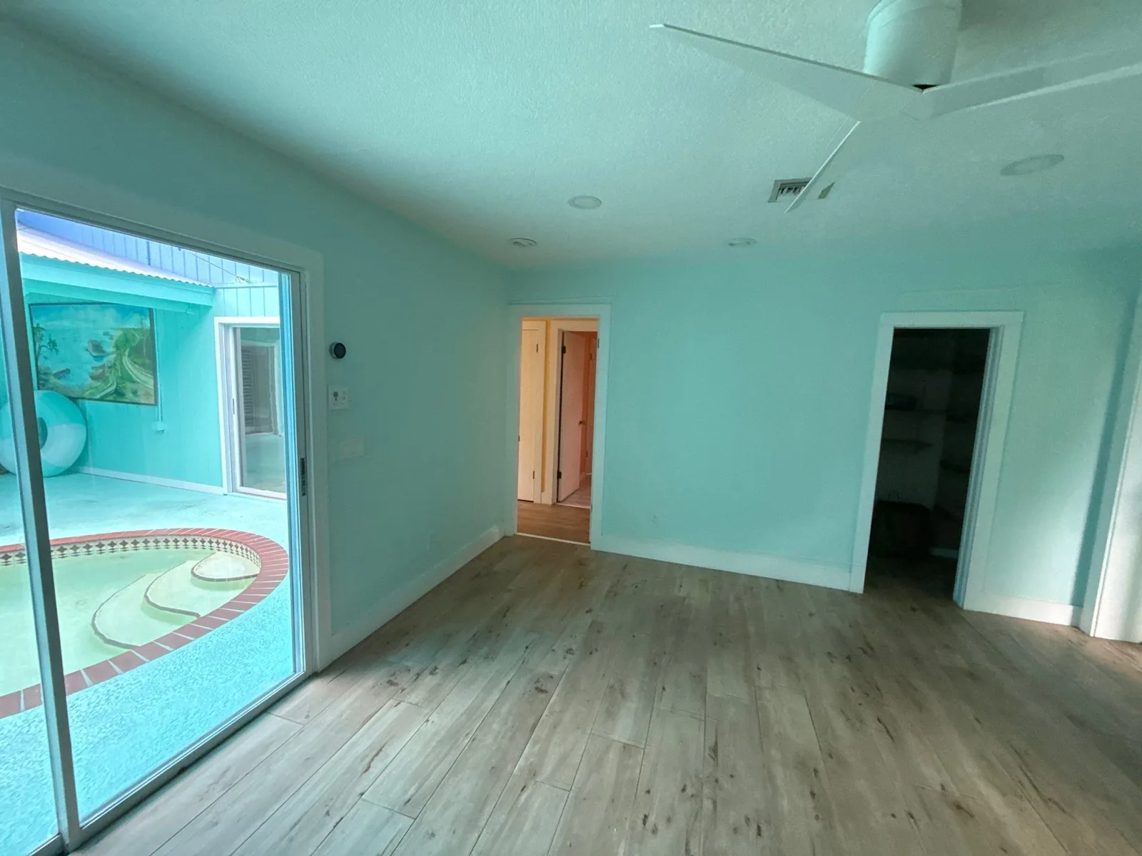 Interior Painting in Jensen Beach, Florida. Empty room with light aqua painted walls and ceiling, light wood-look flooring and a sliding glass door to a screened pool.