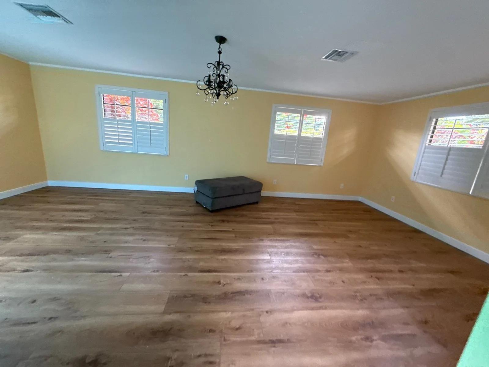 Interior Painting in Jensen Beach, Florida. Empty room with yellow walls, white baseboards and ceiling, plantation-shuttered windows and wood-look flooring.